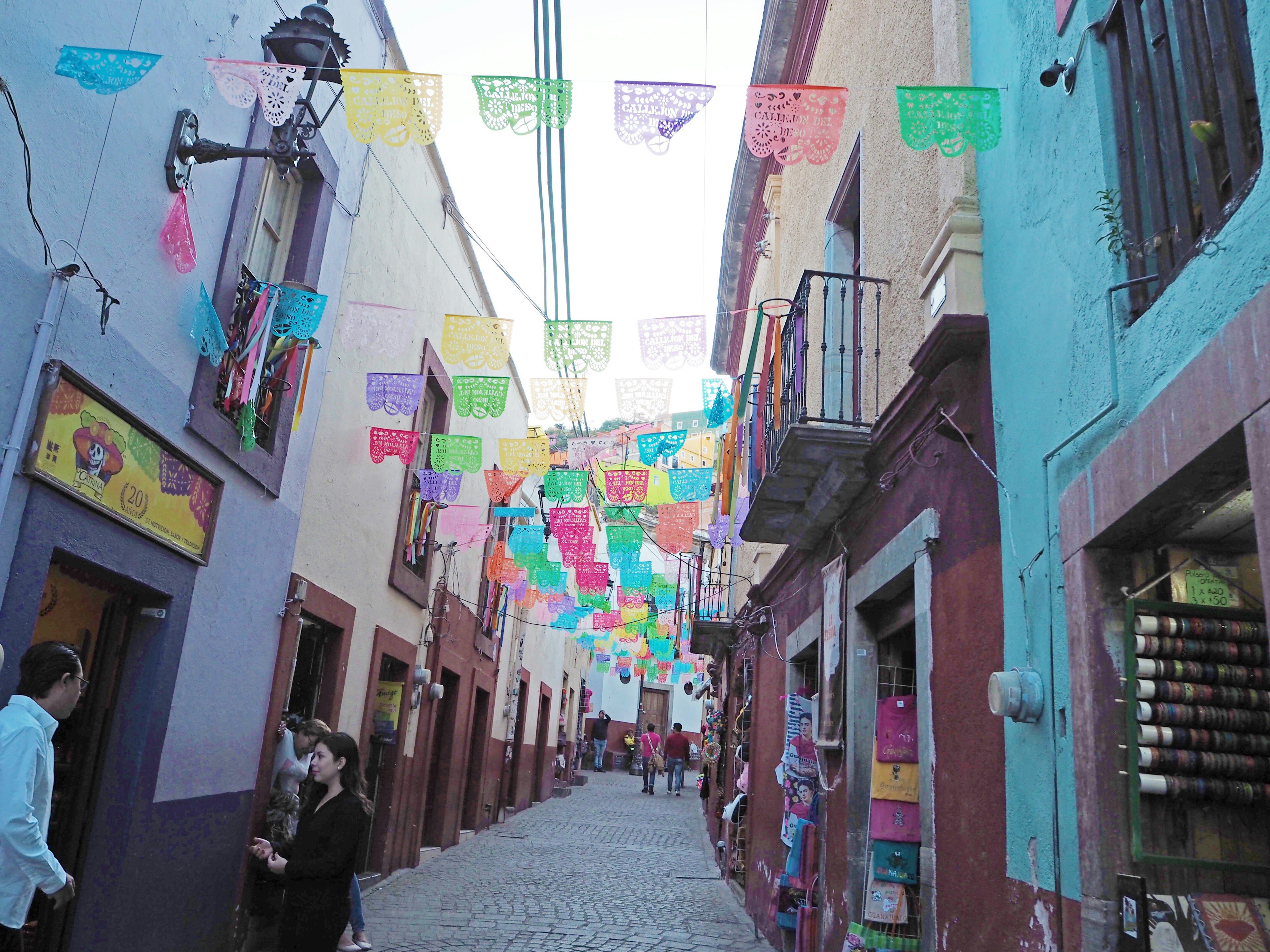 Dekorasi papel picado berwarna-warni menggantung di atas jalan yang ramai