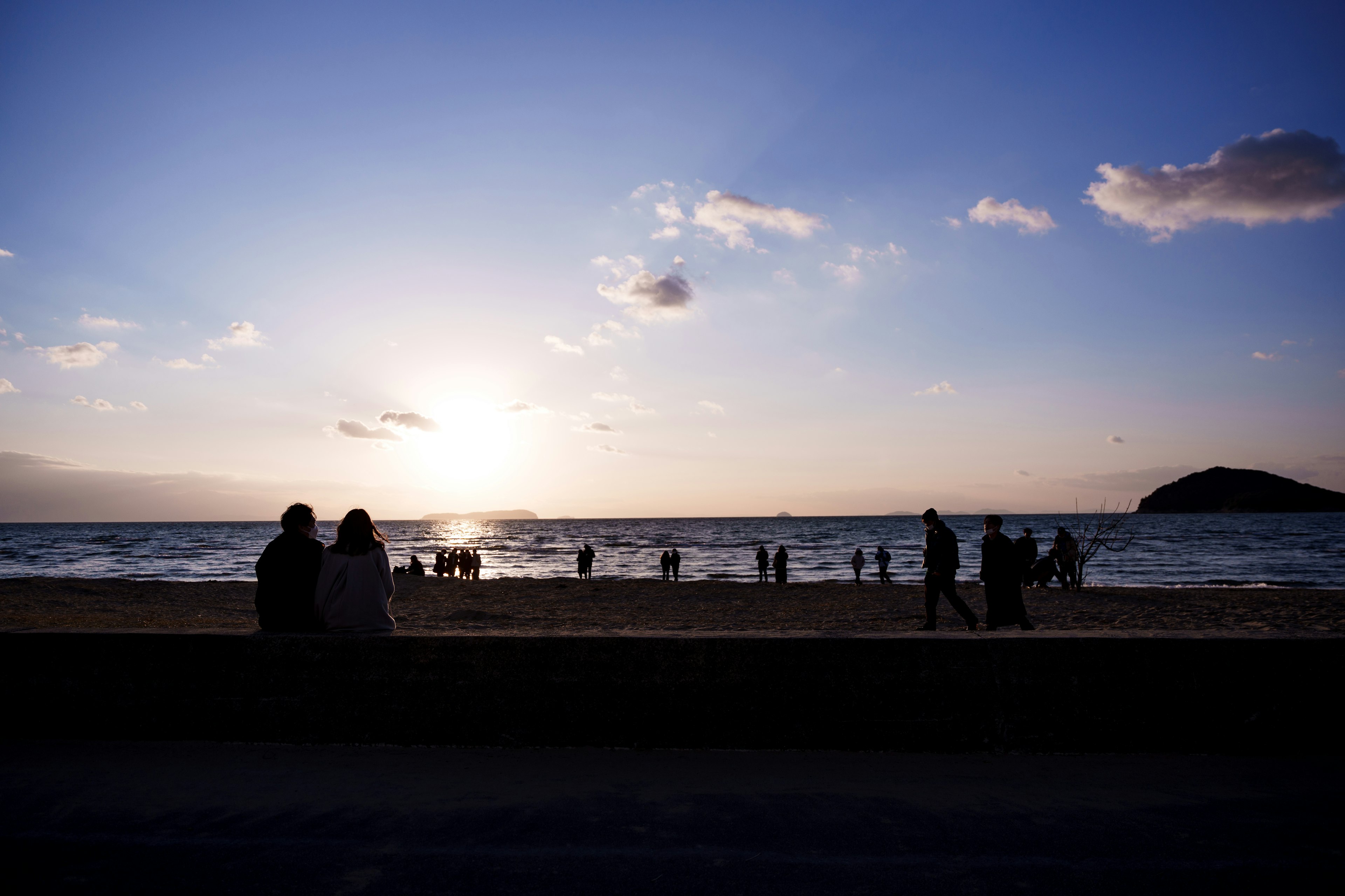 Siluetas de una pareja y personas disfrutando del atardecer en la playa