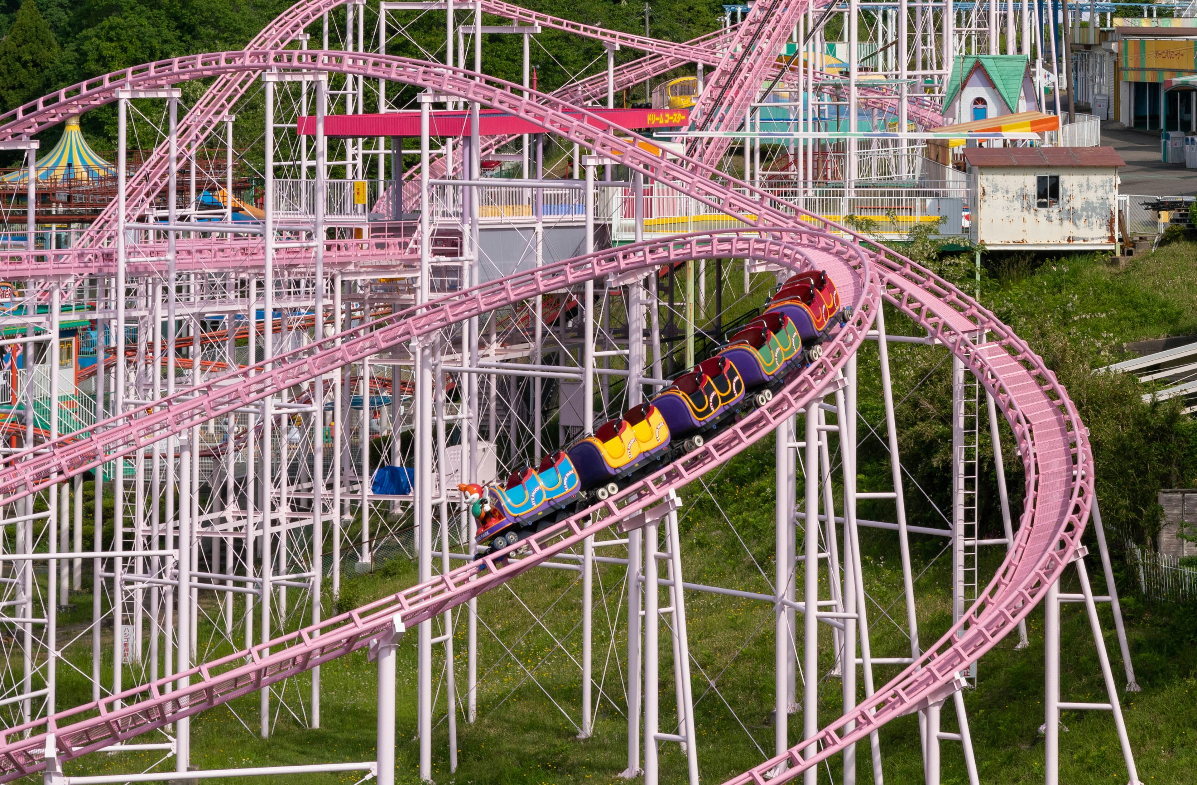 Sebuah roller coaster merah muda melingkar di udara dengan penumpang yang menikmati perjalanan