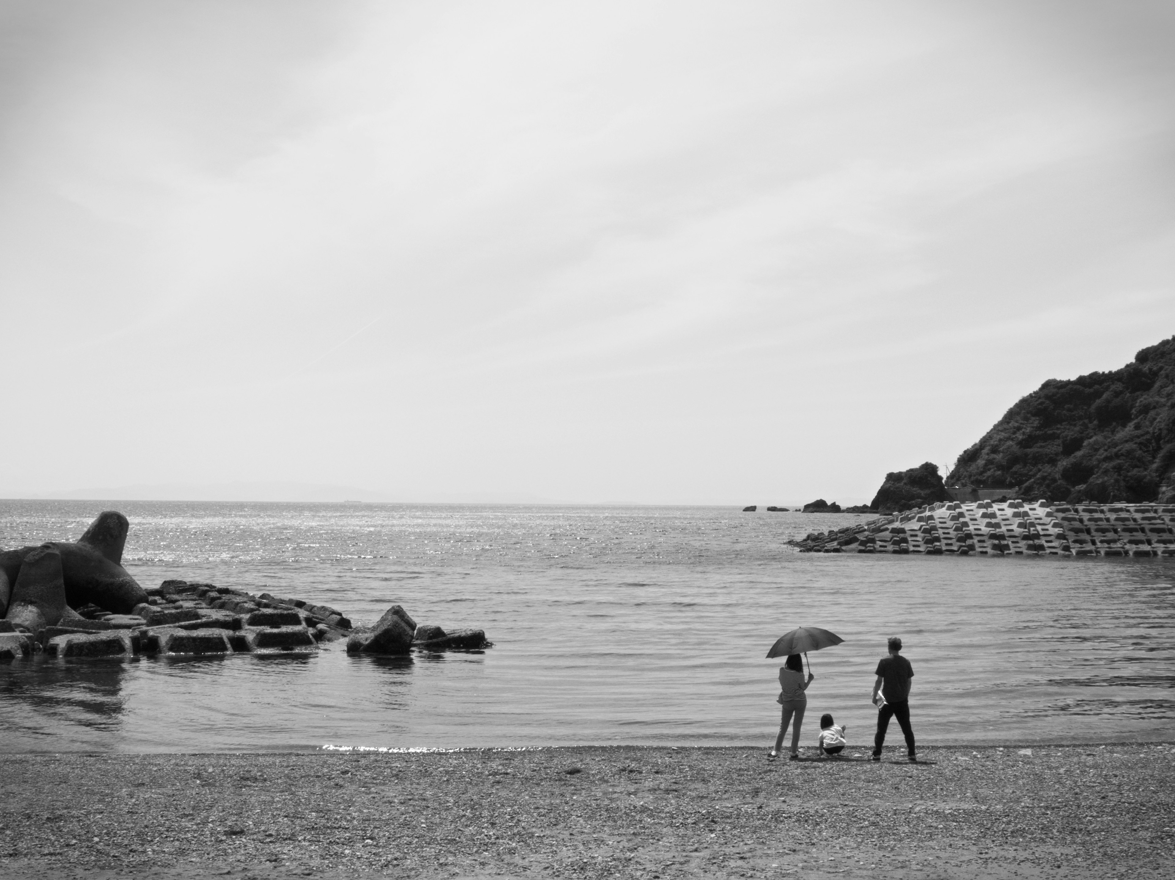 Ein Paar steht mit einem Regenschirm am Strand in Schwarzweiß