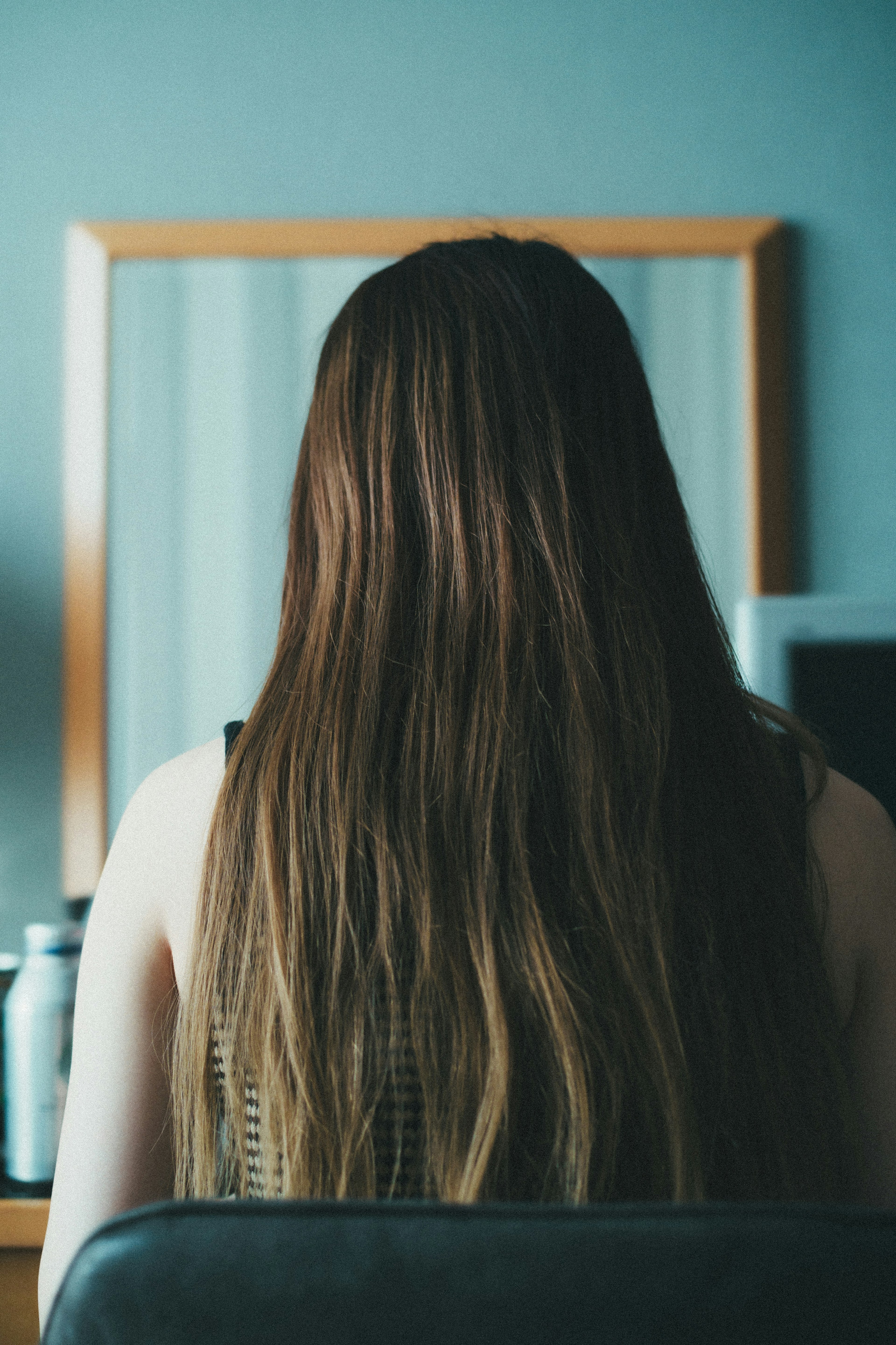 A woman sitting with her back to the camera in front of a mirror