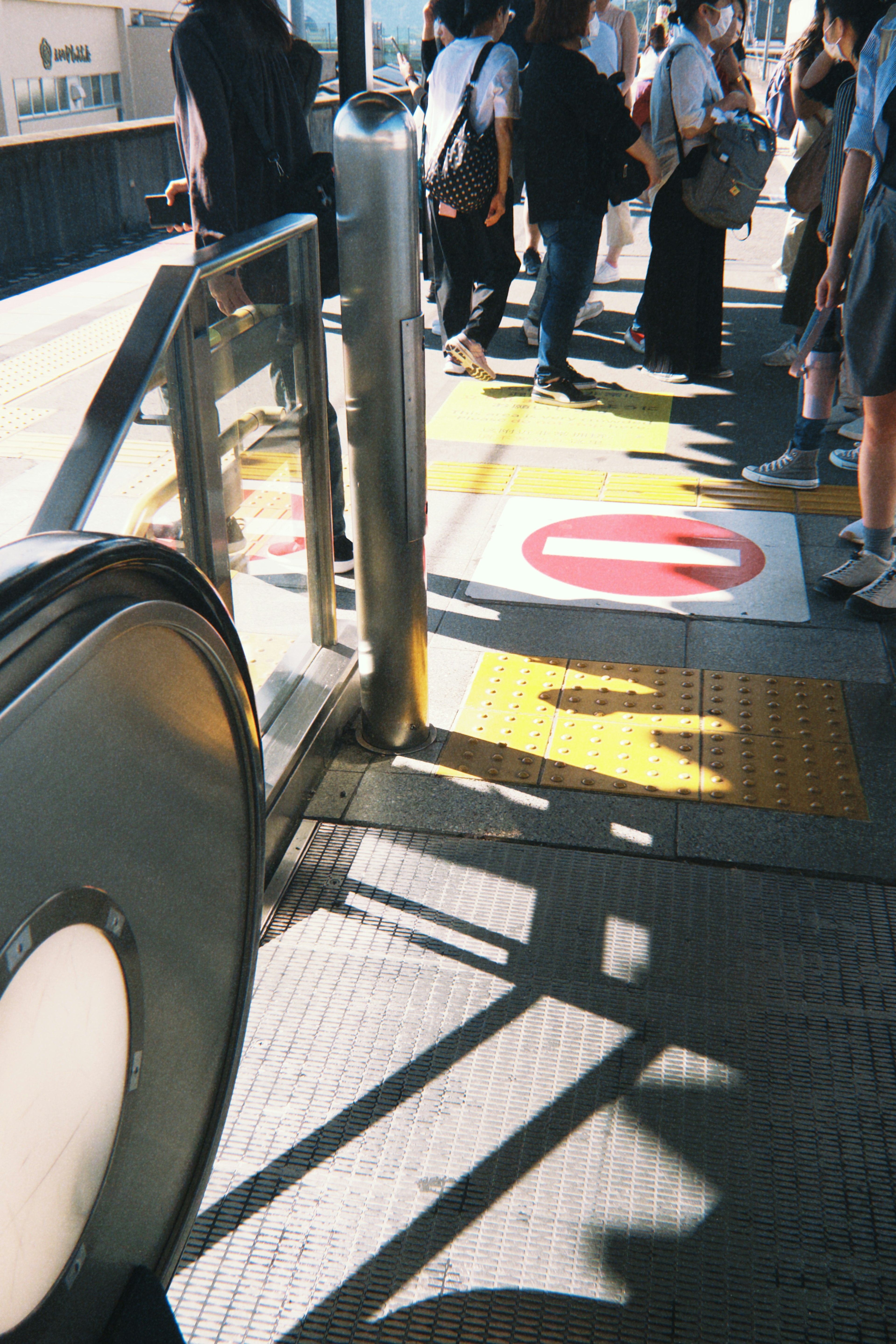 Teil einer Bahnsteigplattform mit einer Rolltreppe und wartenden Menschen