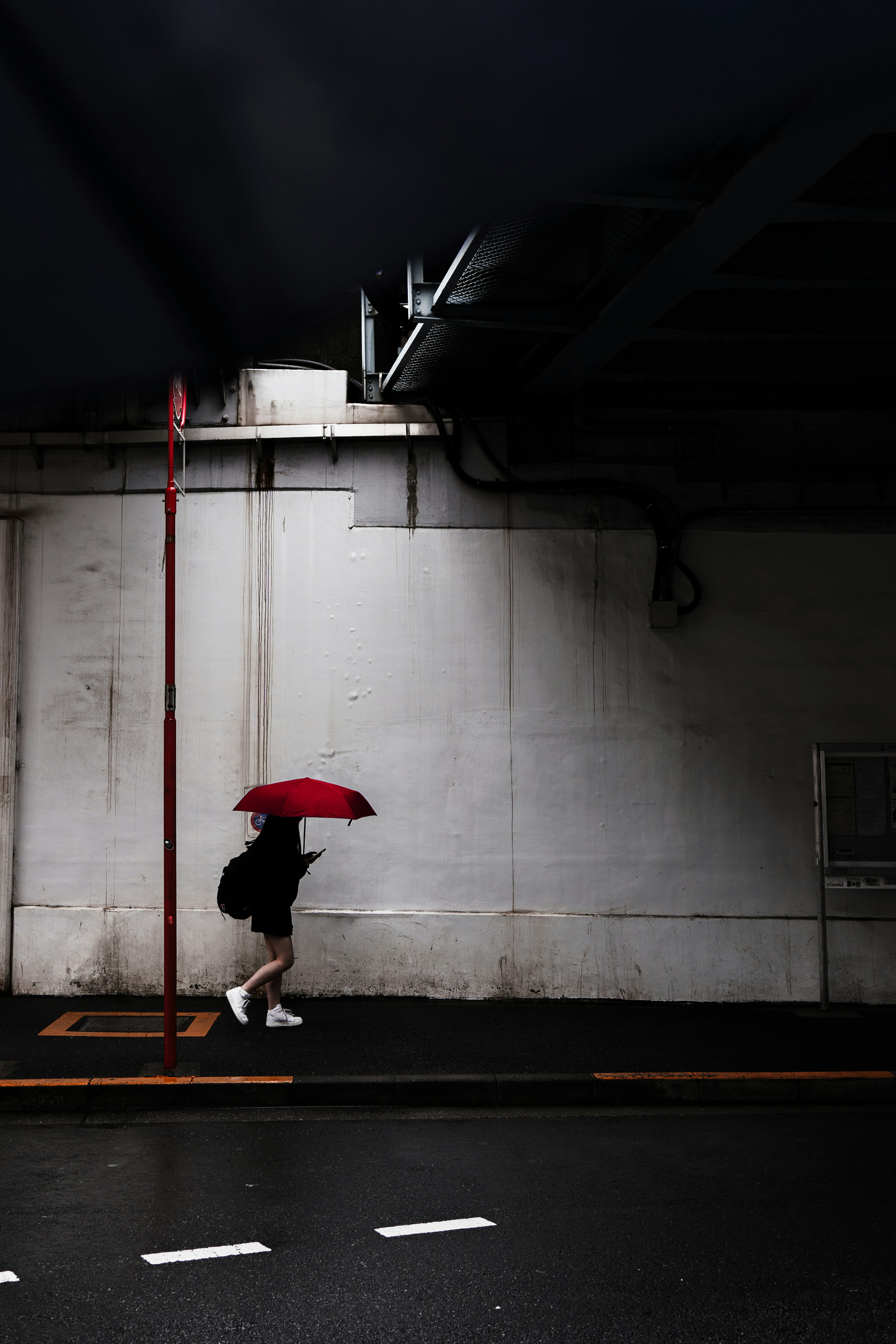 Silhouette einer Person, die mit einem roten Regenschirm unter einem dunklen Himmel geht