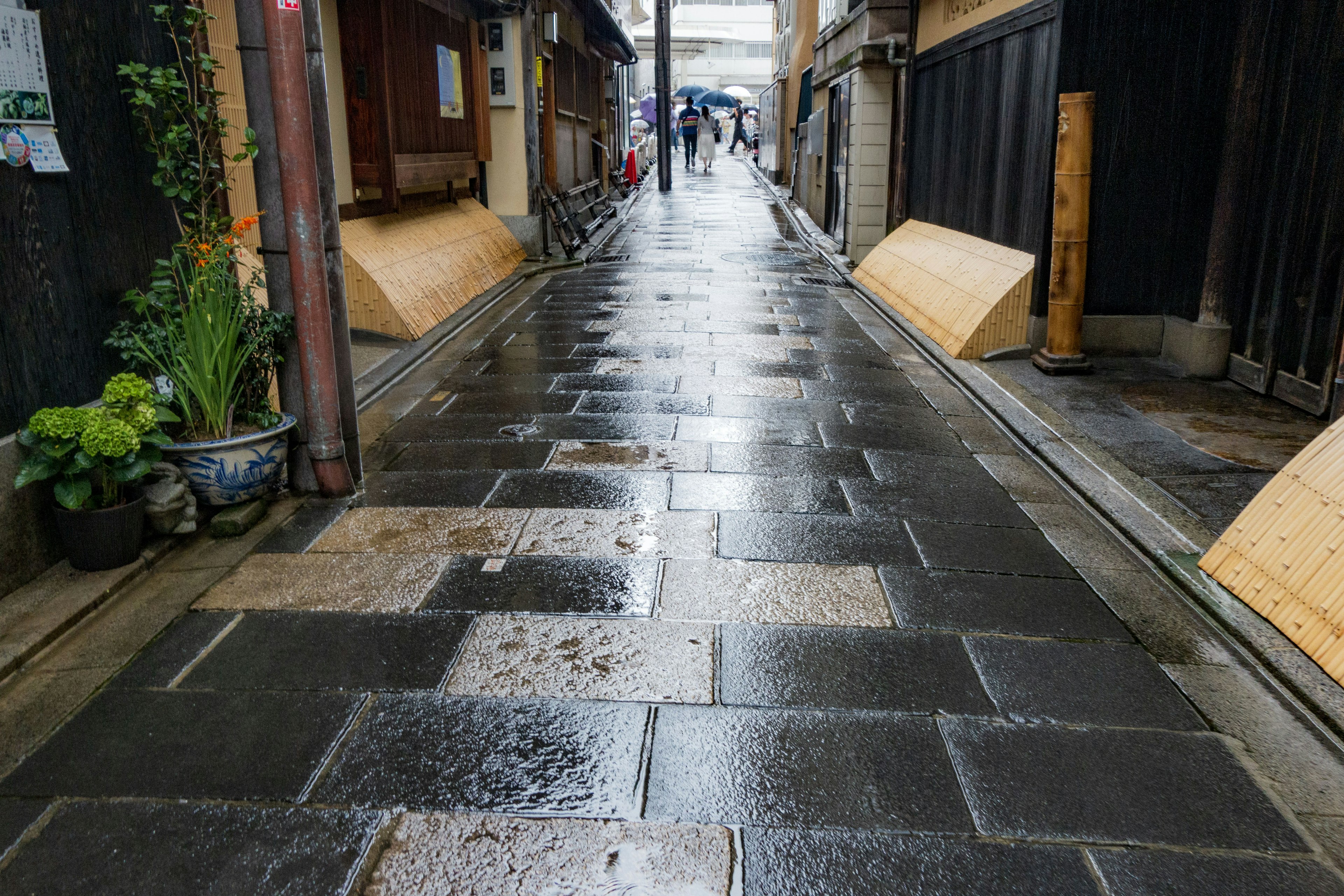 Eine Ansicht einer schmalen, regennassen Steinpflastergasse mit traditionellen japanischen Gebäuden auf beiden Seiten