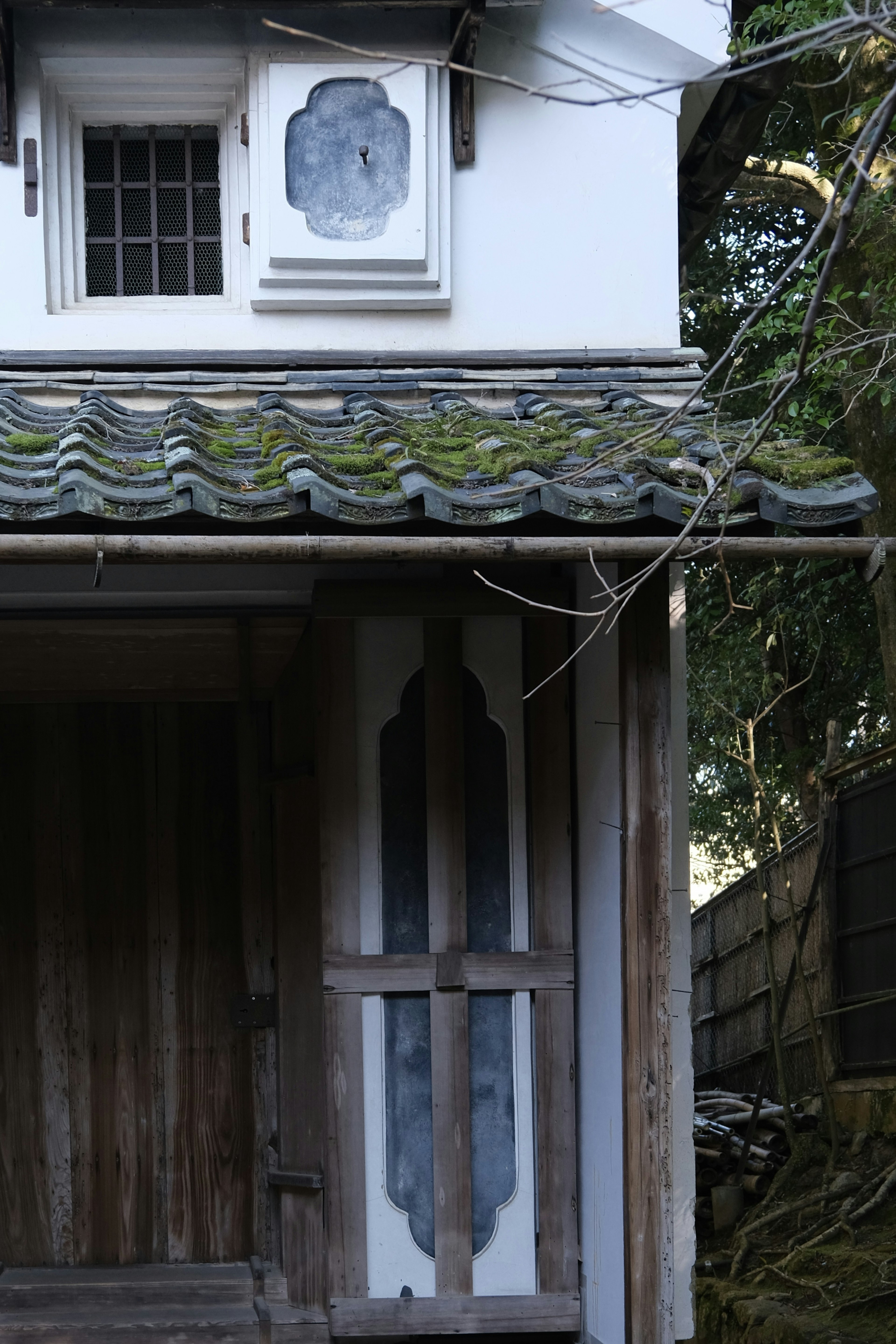 Exterior of an old Japanese building with a tiled roof and wooden doors featuring unique window designs