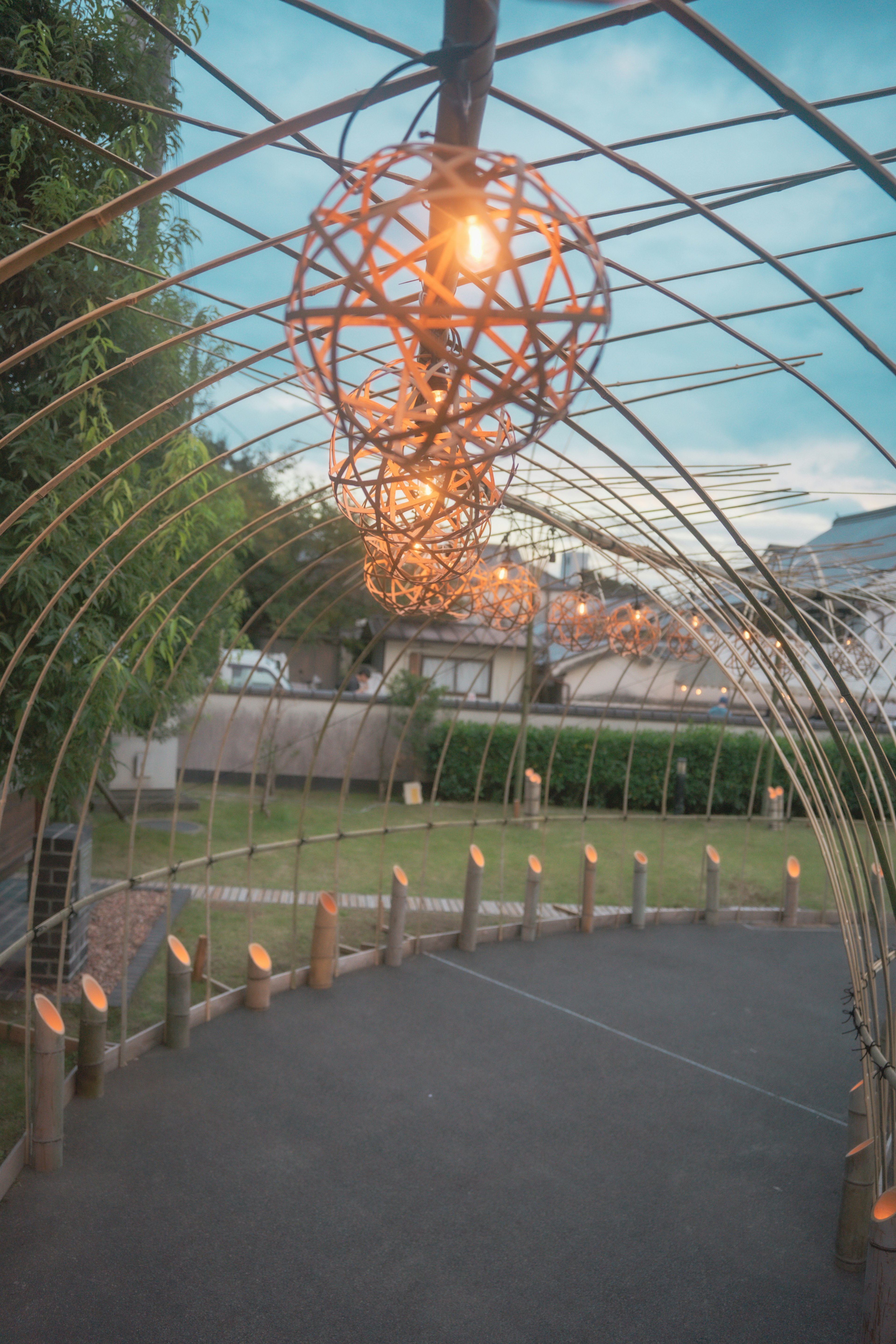 Archway structure with hanging lights surrounded by greenery and a clear sky