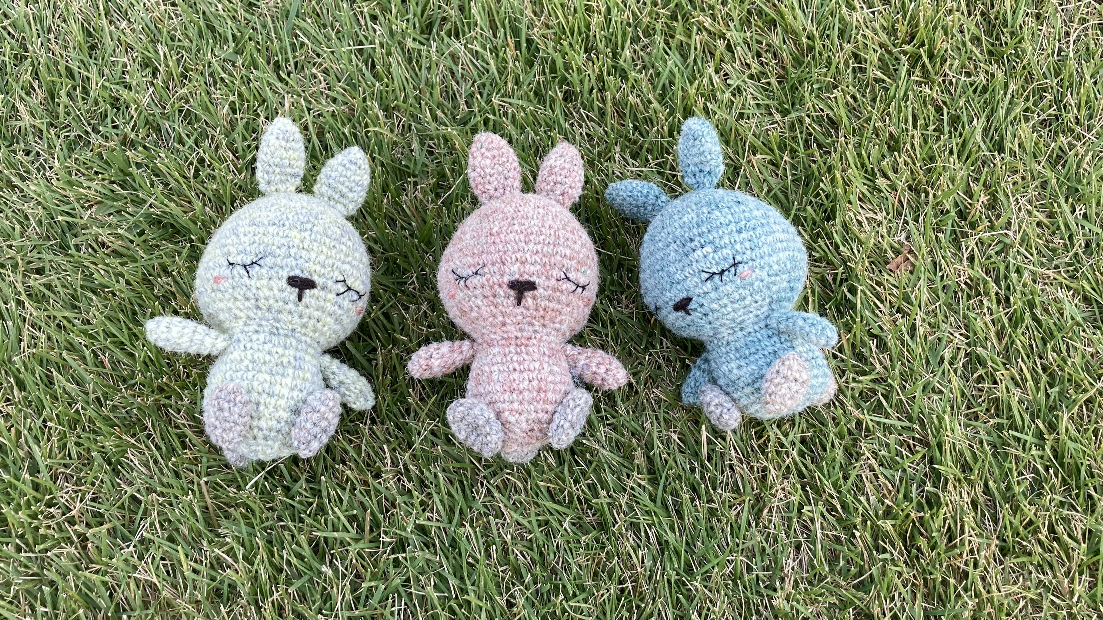 Tiga kelinci plush lucu berwarna pastel duduk di atas rumput hijau