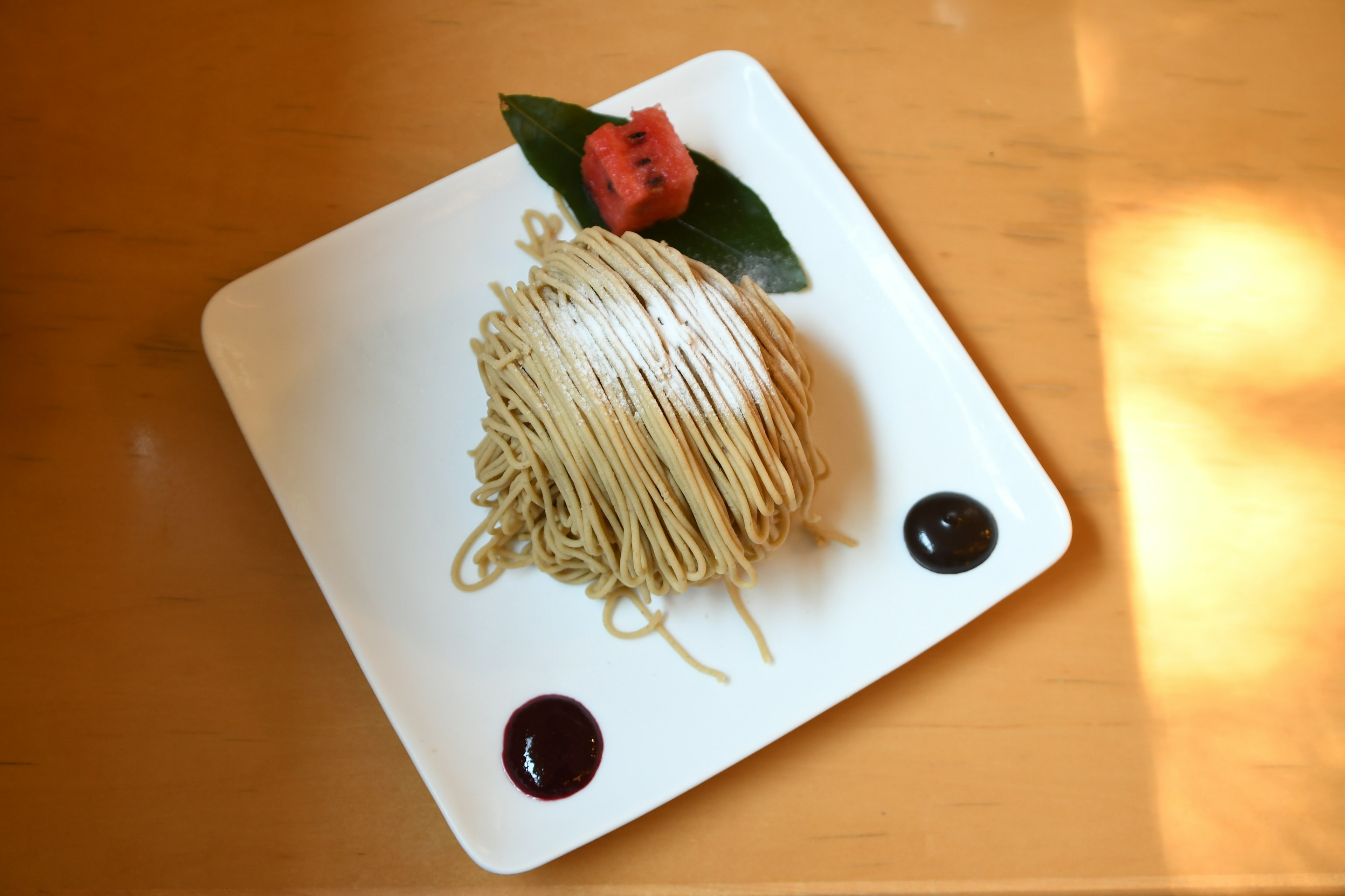 Thin pasta arranged on a white plate with green leaves and a red flower garnish