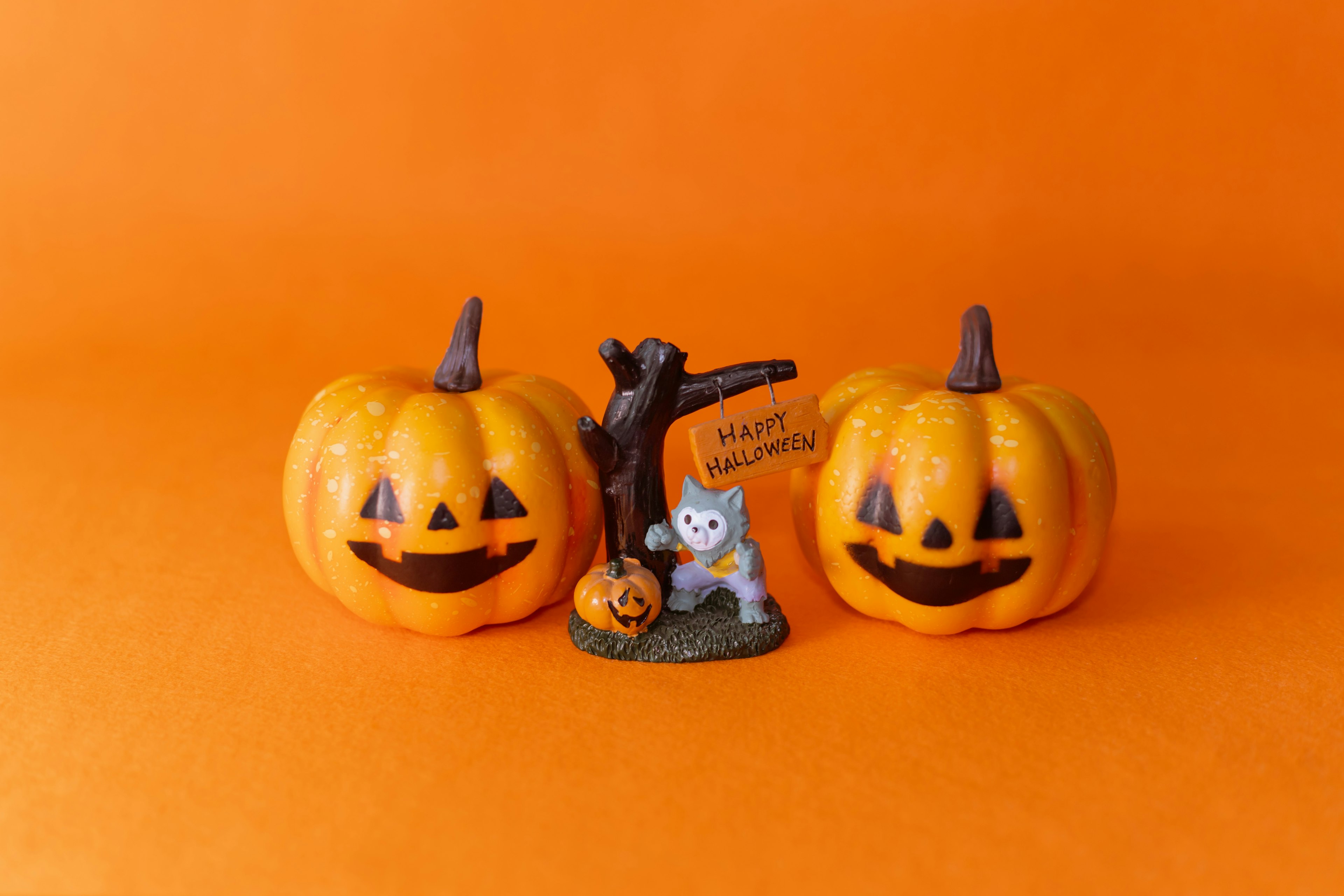 Dos calabazas sonrientes con una pequeña decoración de gato blanco sobre un fondo naranja