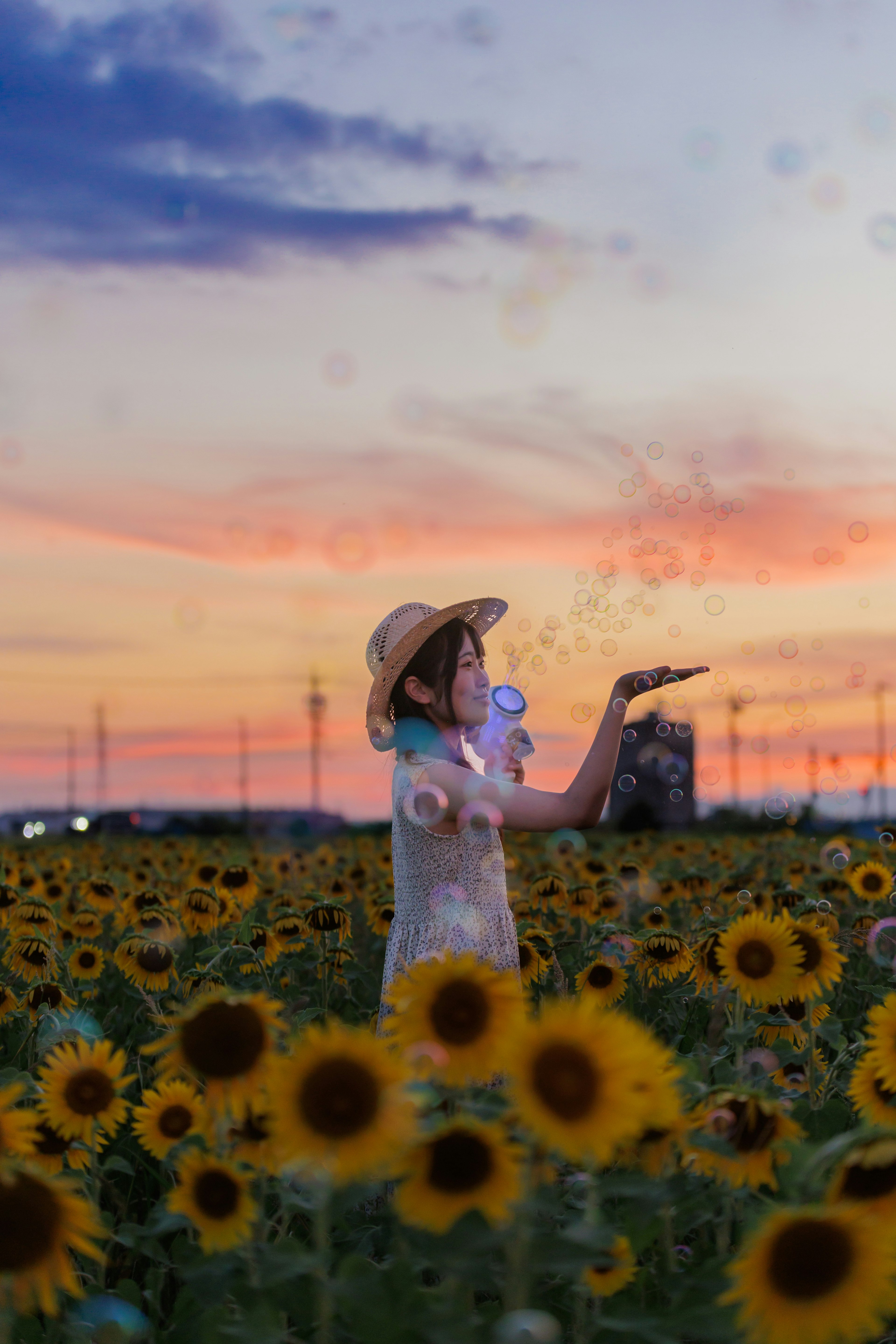 夕焼けの中でひまわり畑に立つ女性が風船を持っている