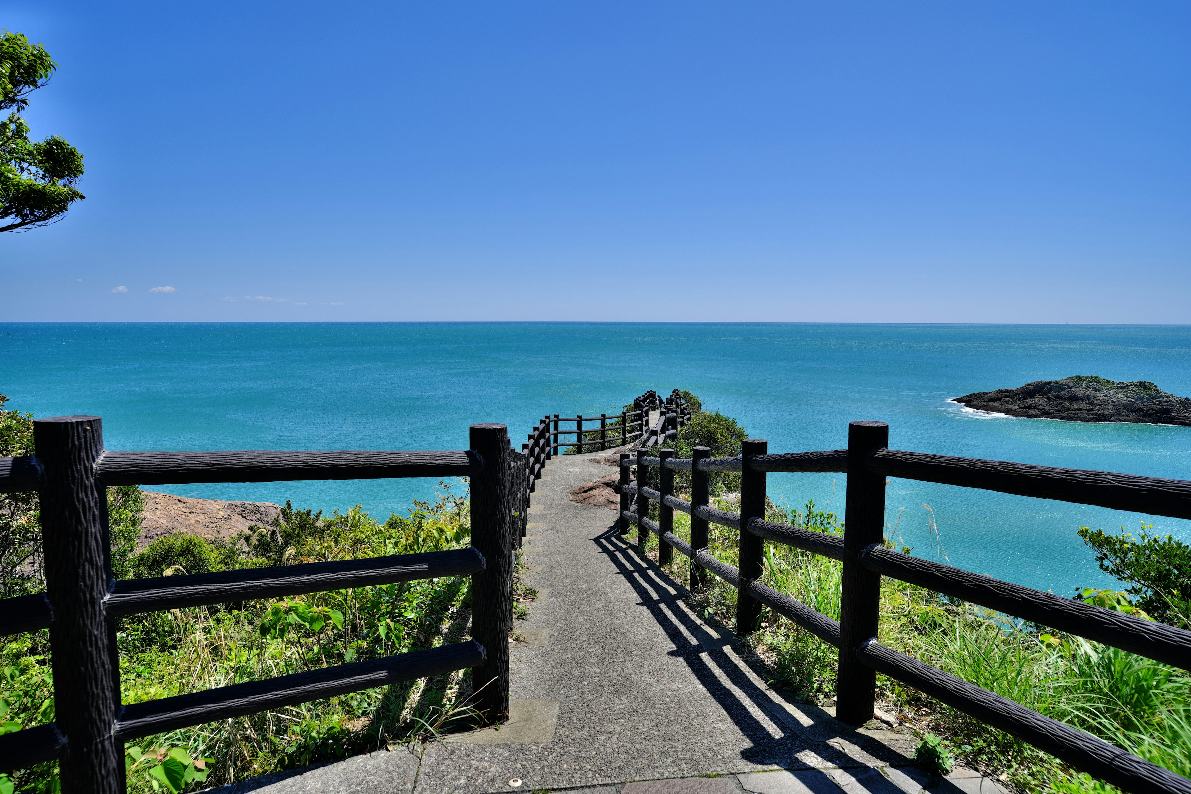 Sentier avec rambarde en bois surplombant la mer et le ciel bleus