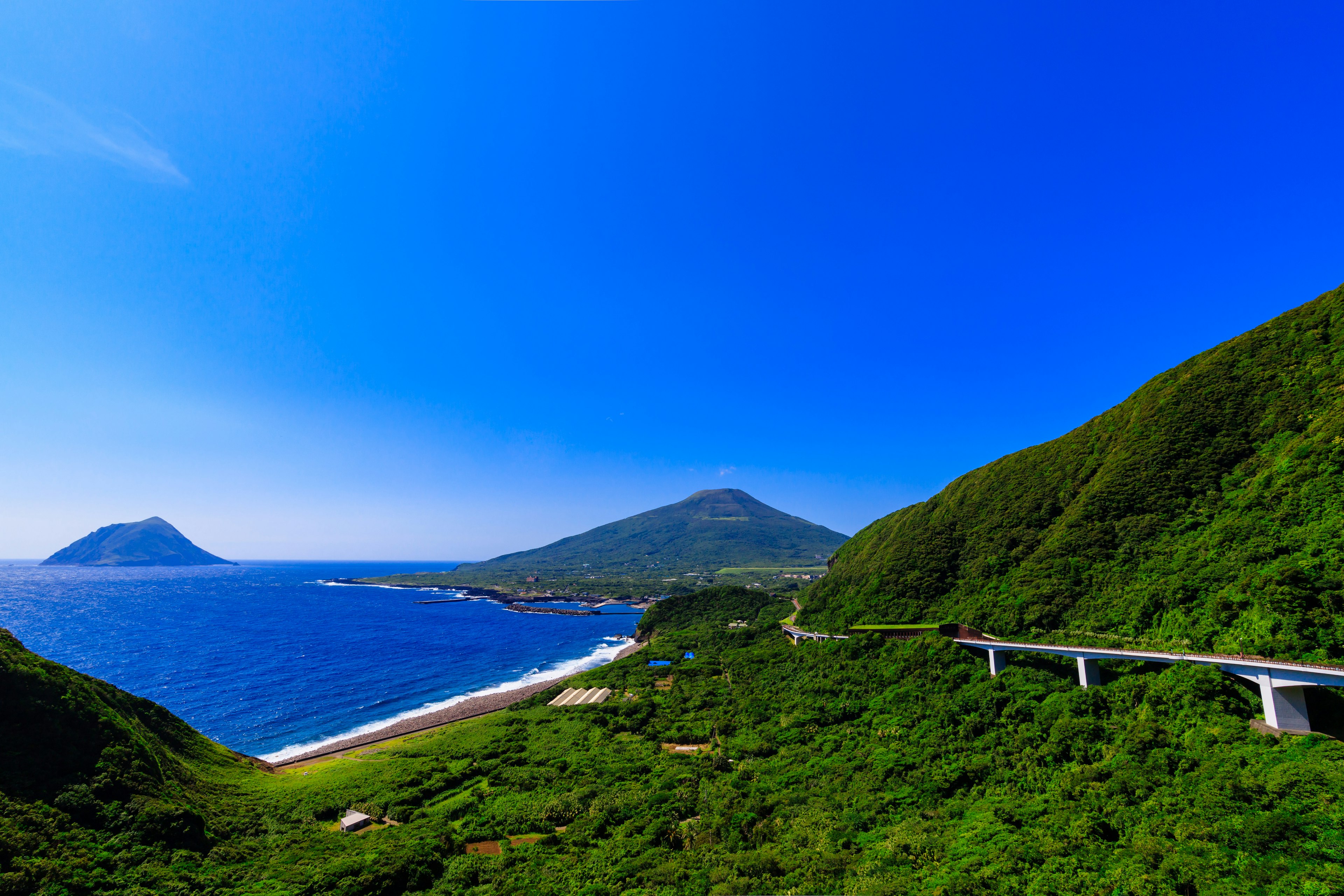 Paesaggio costiero panoramico con montagne verdi e cielo blu chiaro