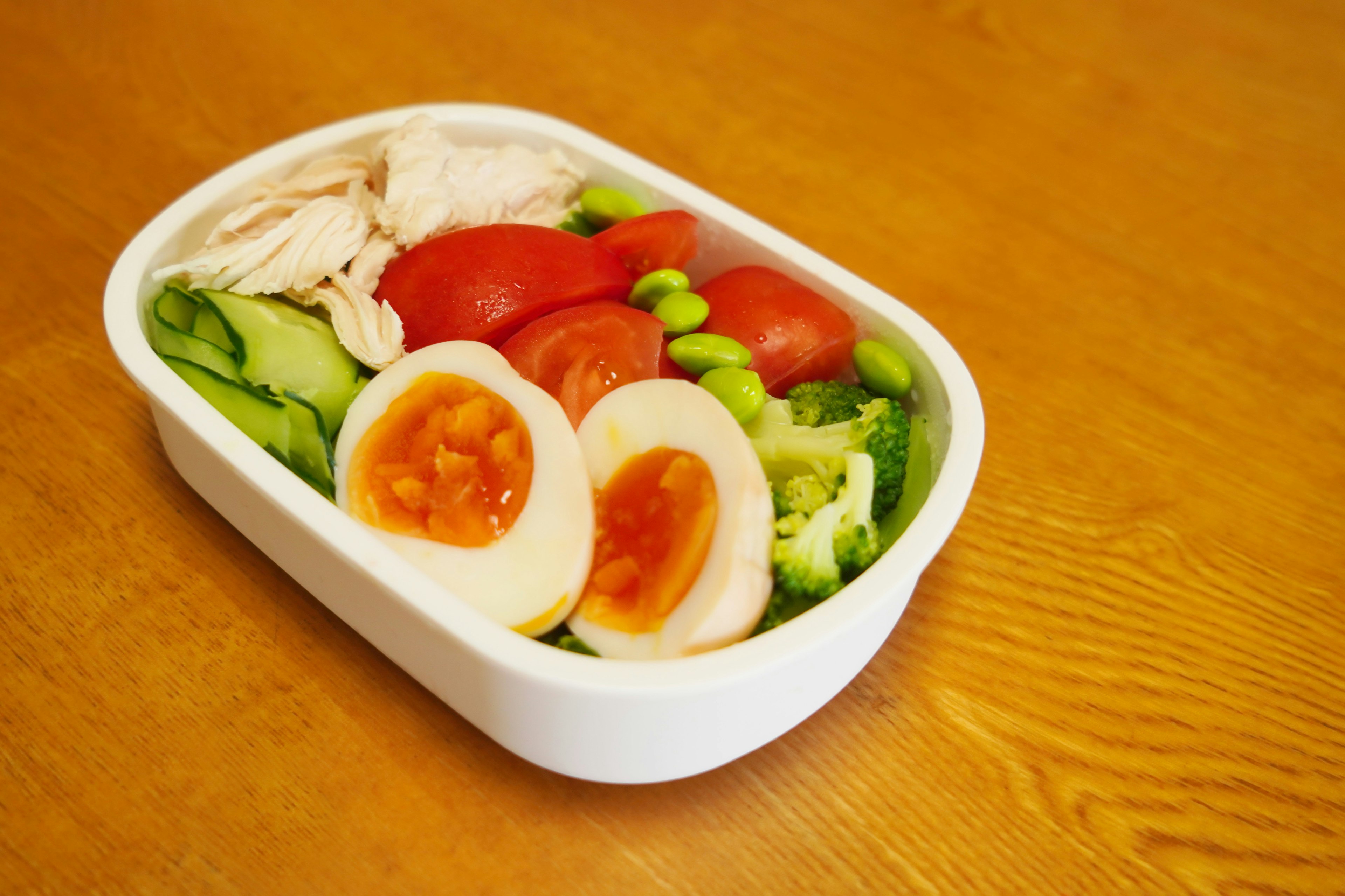 Salad bowl in a white container with sliced chicken tomatoes boiled eggs edamame and cucumber