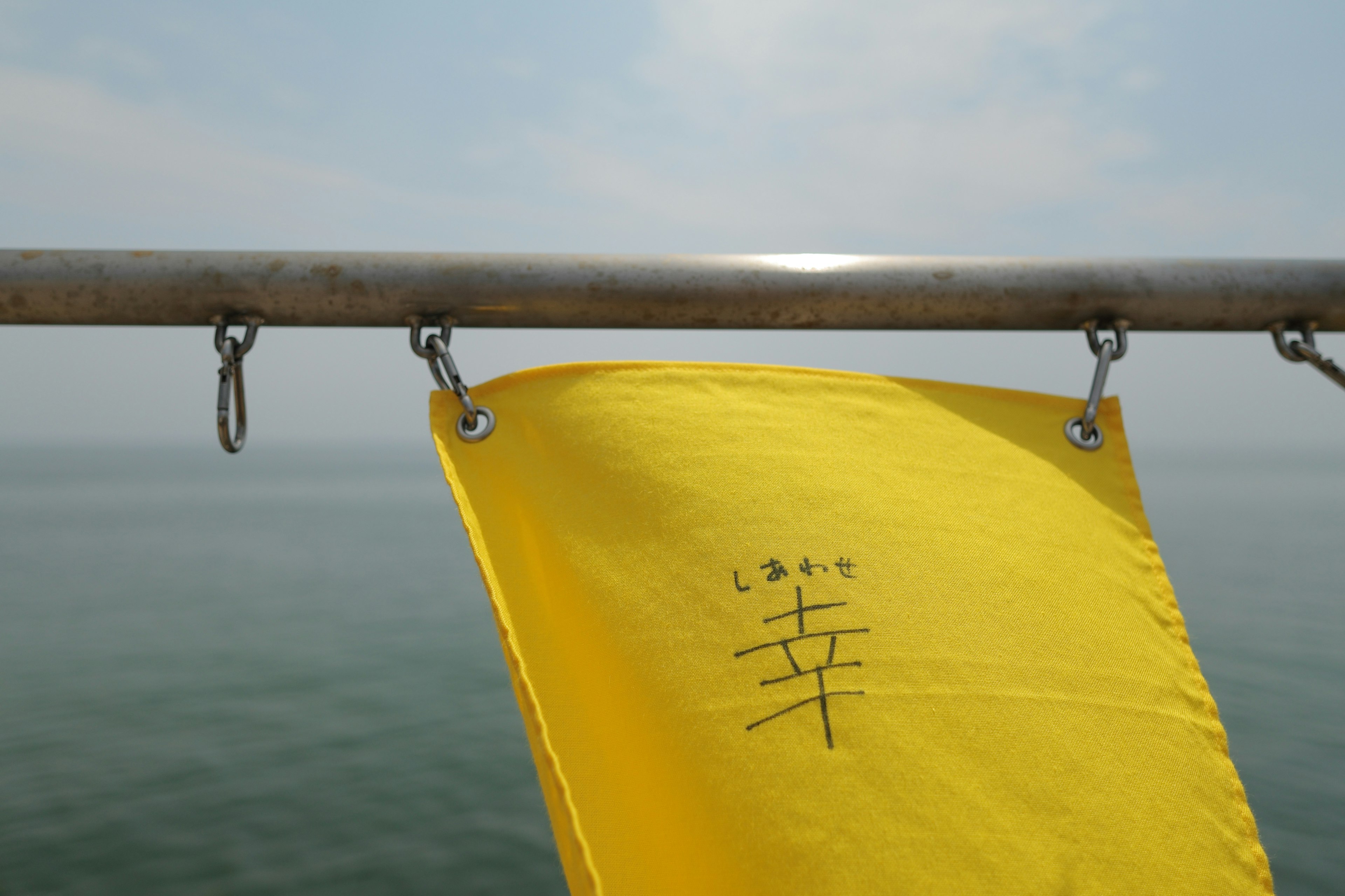 Una bandera amarilla colgada frente al mar con el carácter kanji para felicidad