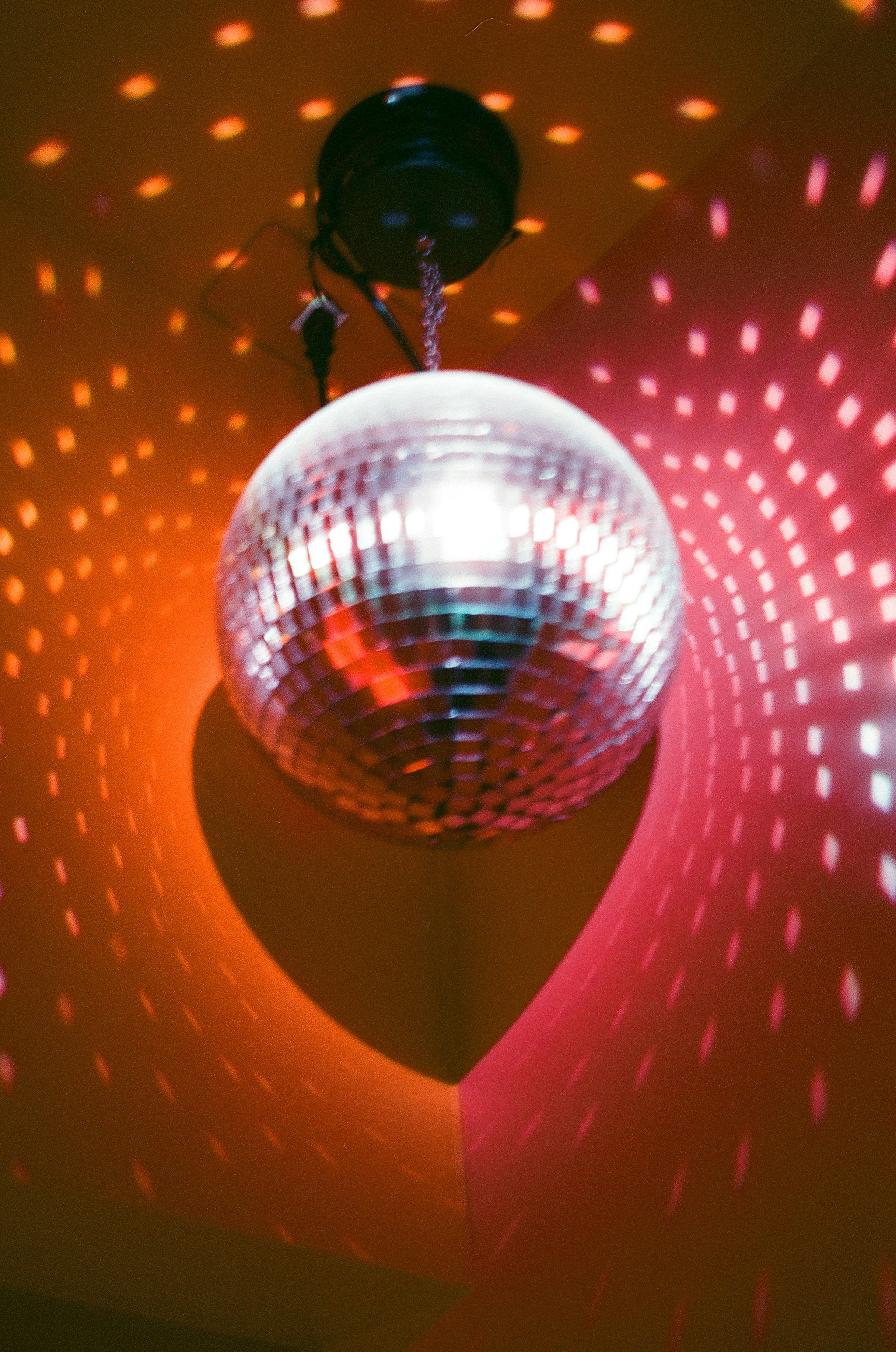 A disco ball hanging from the ceiling reflecting colorful lights on a red wall