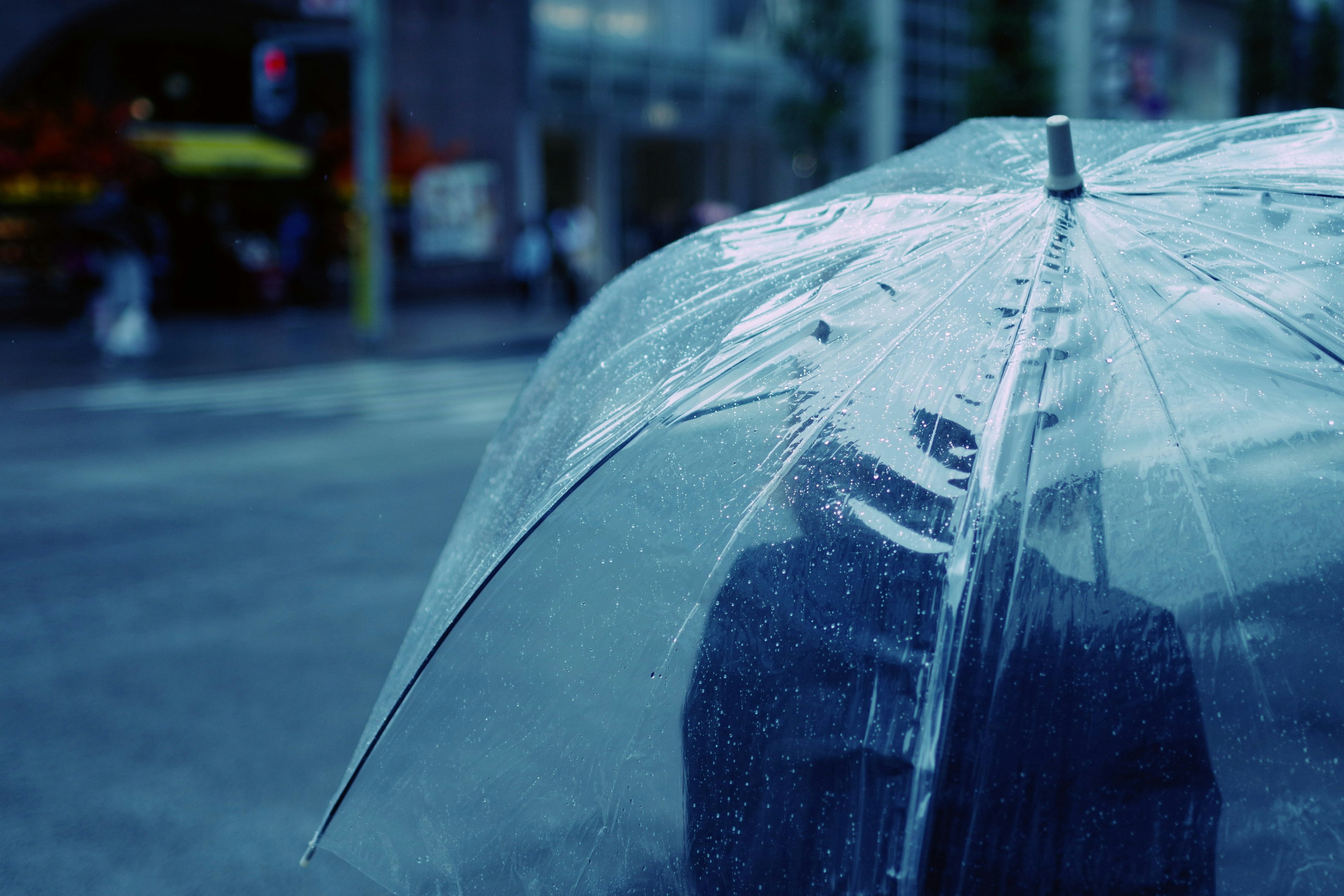 透明な傘の下にいる人の後ろ姿 雨の雫が傘に付いている 都会的な背景