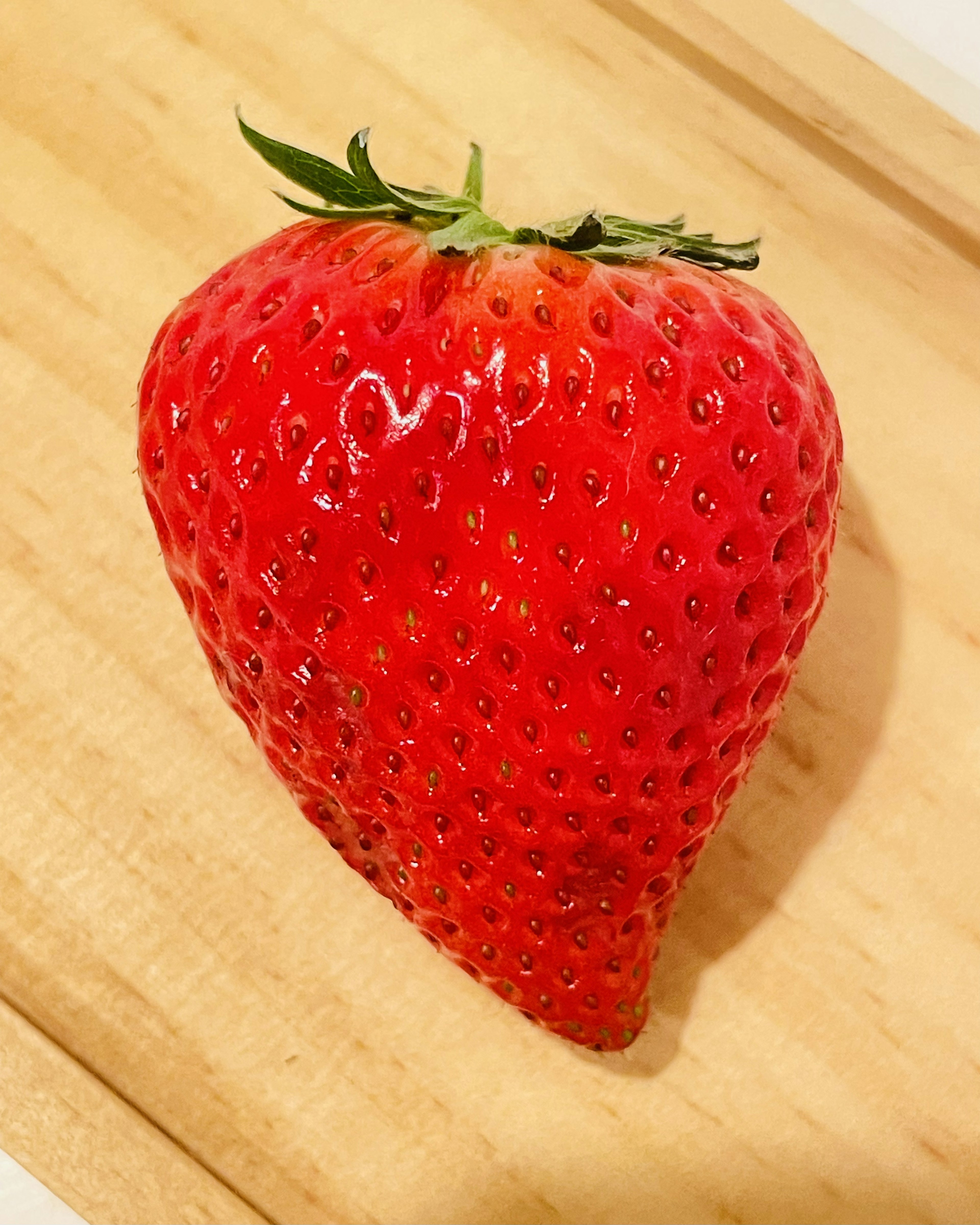 A vibrant red strawberry placed on a wooden board