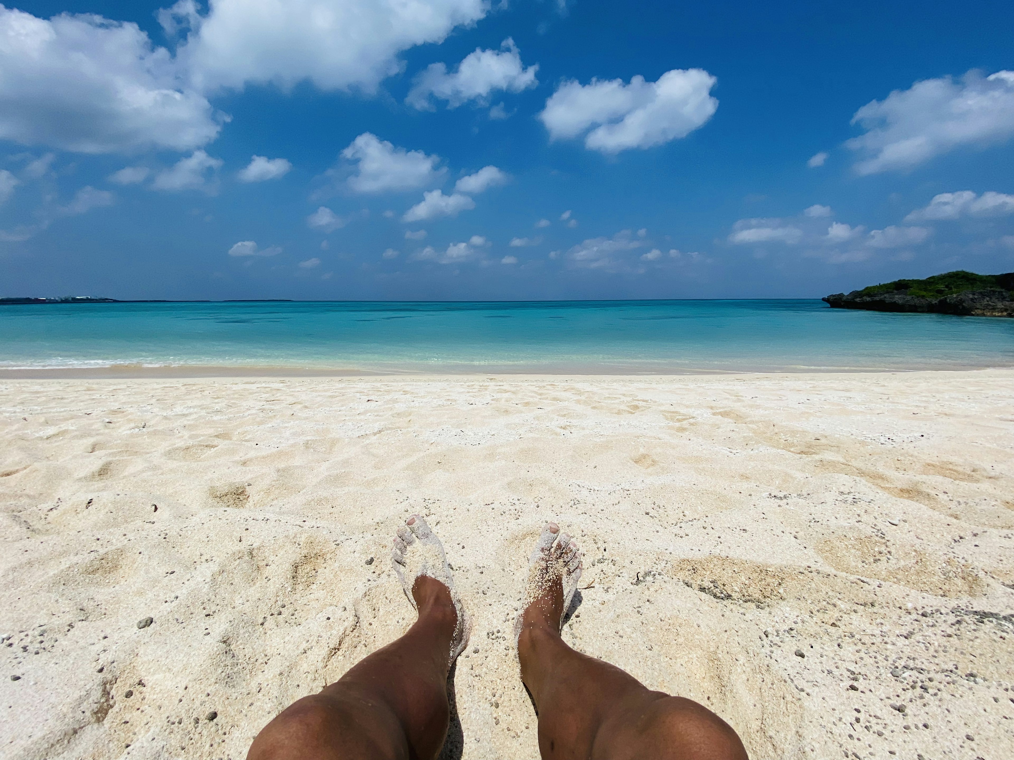 Pemandangan santai kaki di pantai pasir putih dengan lautan biru dan awan