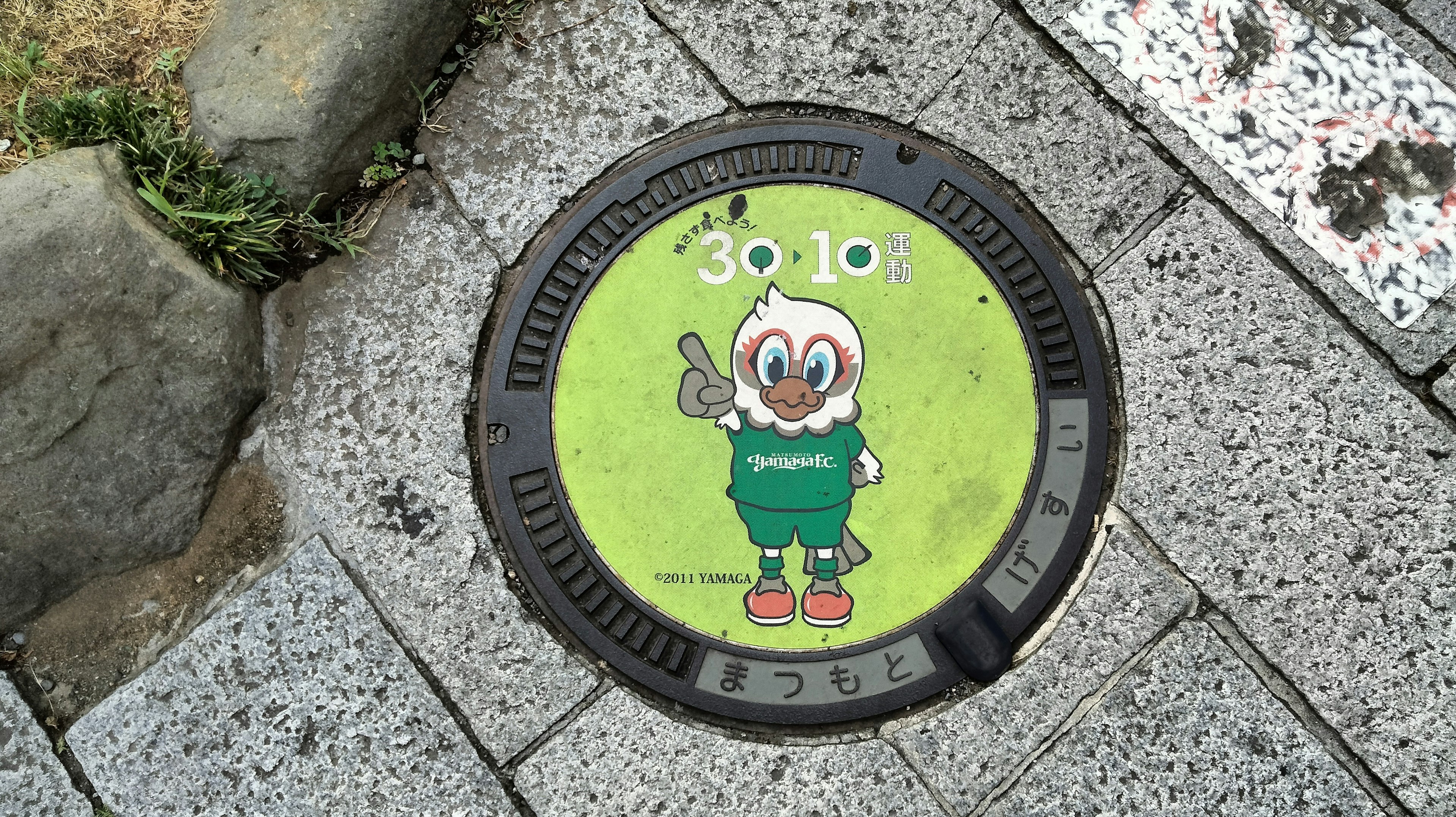 Green manhole cover featuring a cartoon character