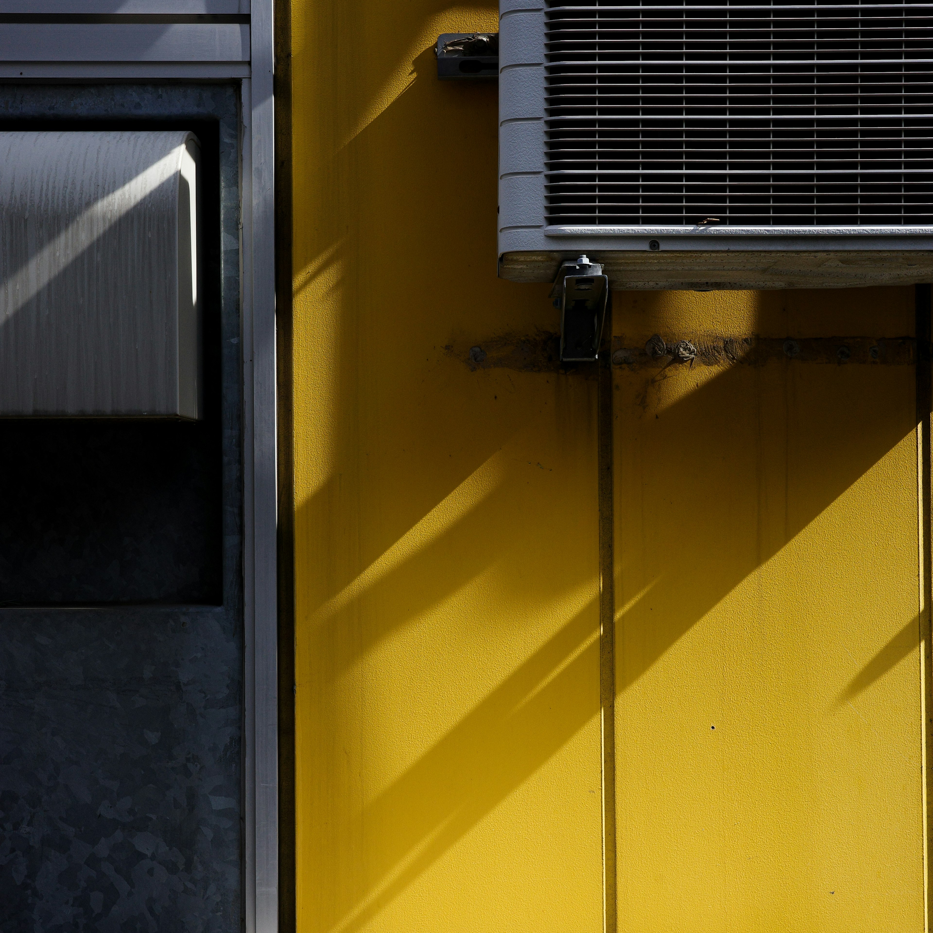 Contrast of air conditioning unit against a yellow wall with shadows