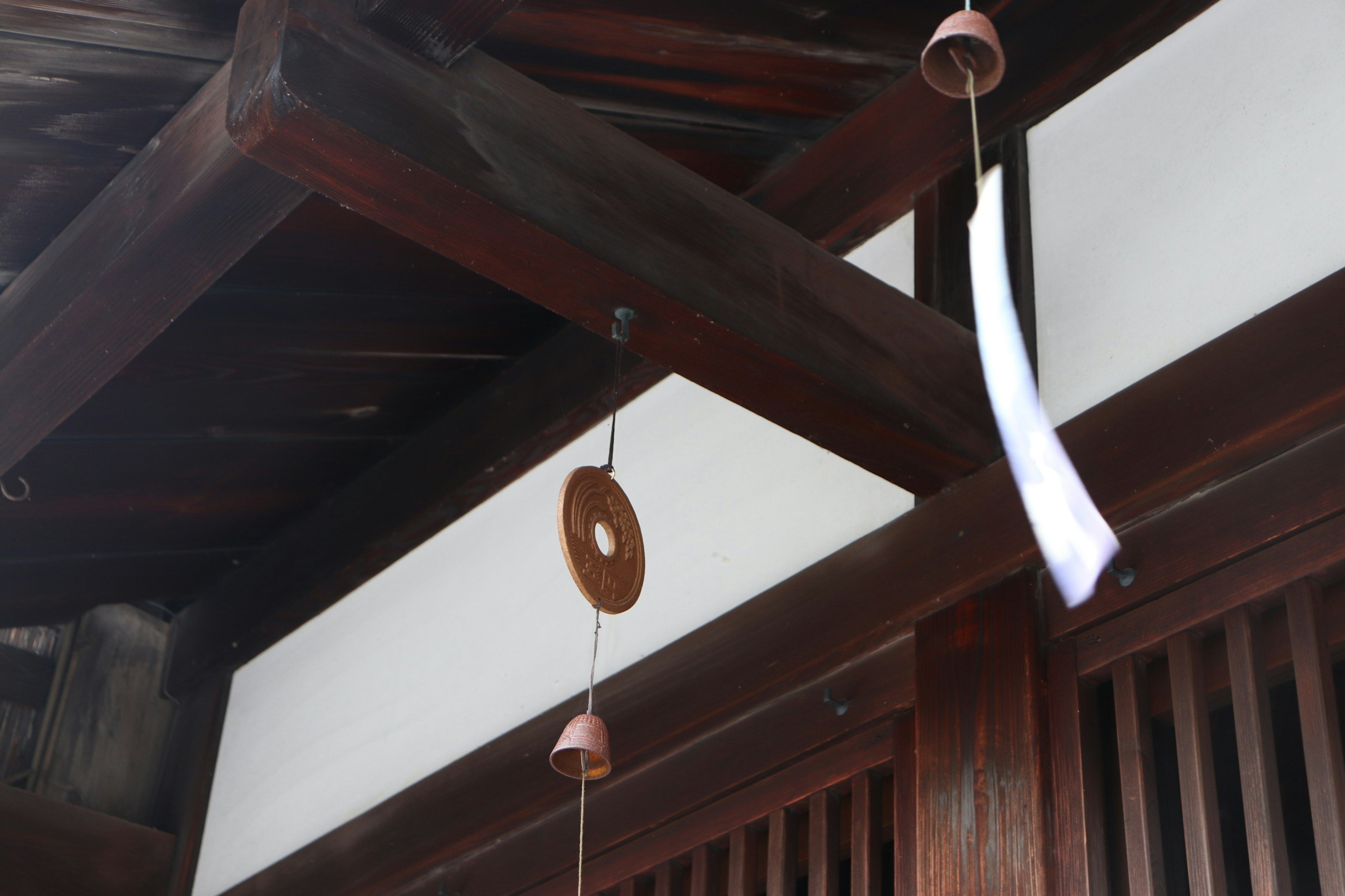 Wind chime and white paper hanging under a wooden roof