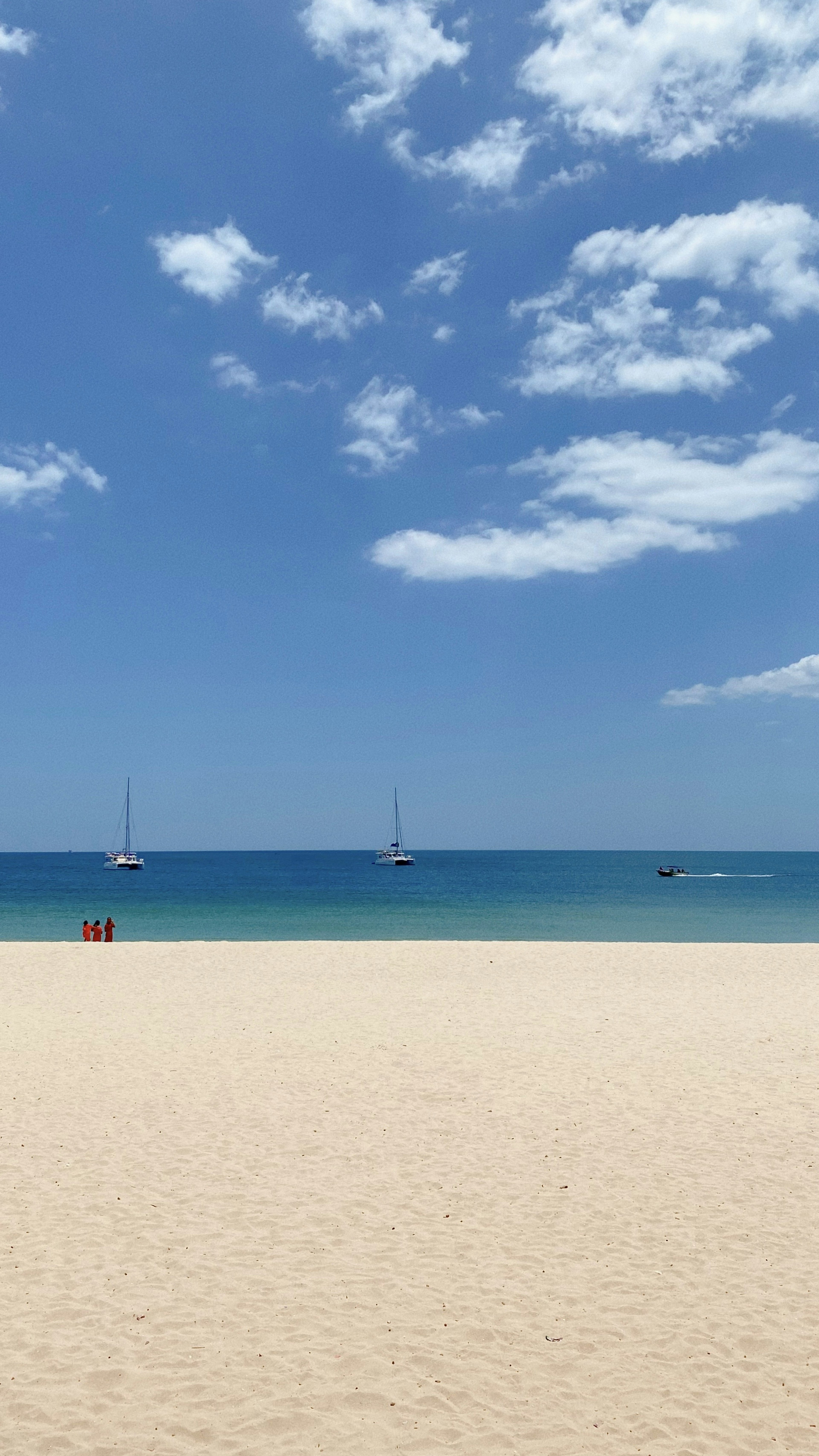 ชายหาดที่มีท้องฟ้าสีฟ้าและมหาสมุทรที่มีเรือใบ