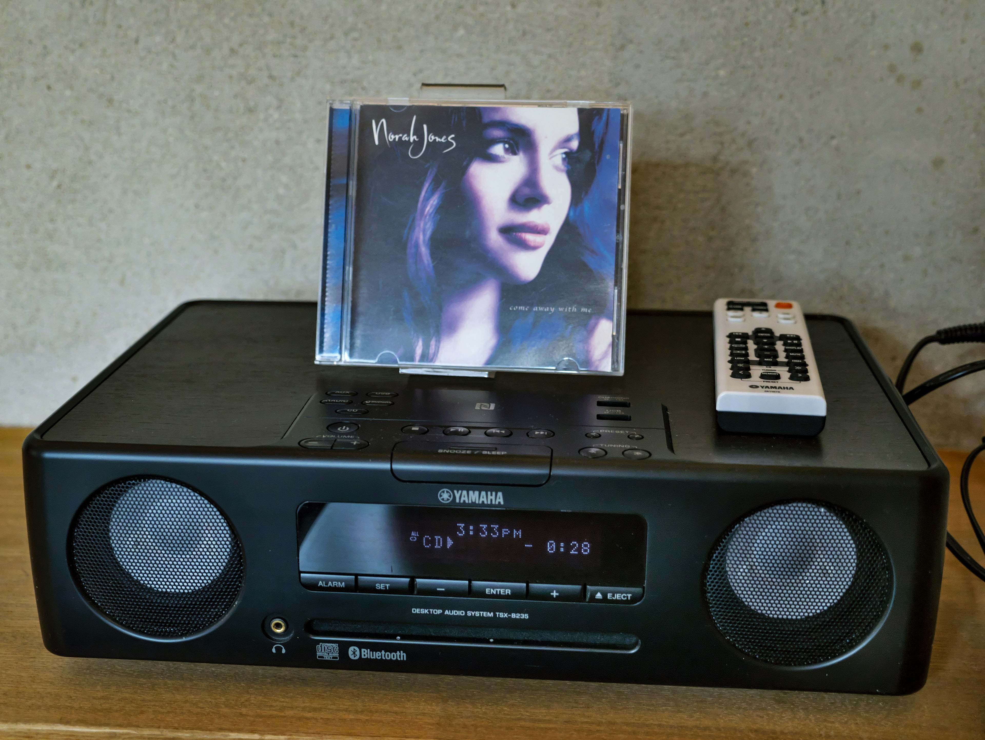 Black CD player with a remote and a CD cover featuring a woman's portrait