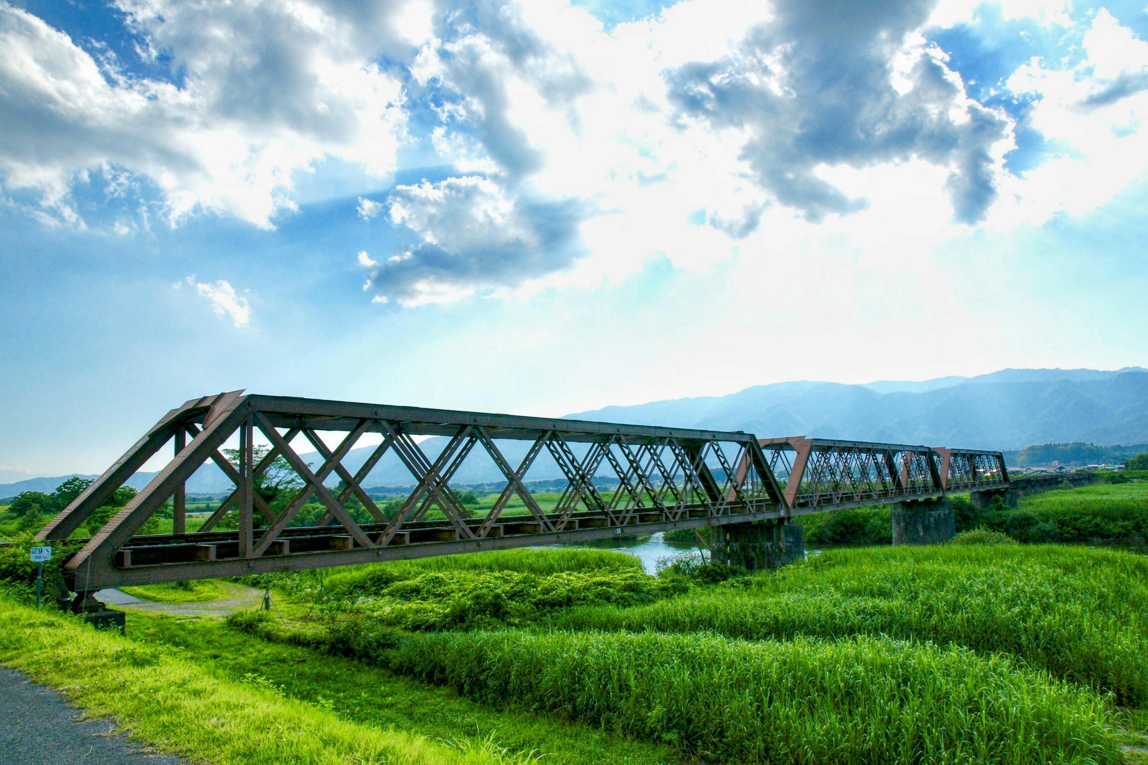 Jembatan kereta api di bawah langit biru dengan ladang hijau