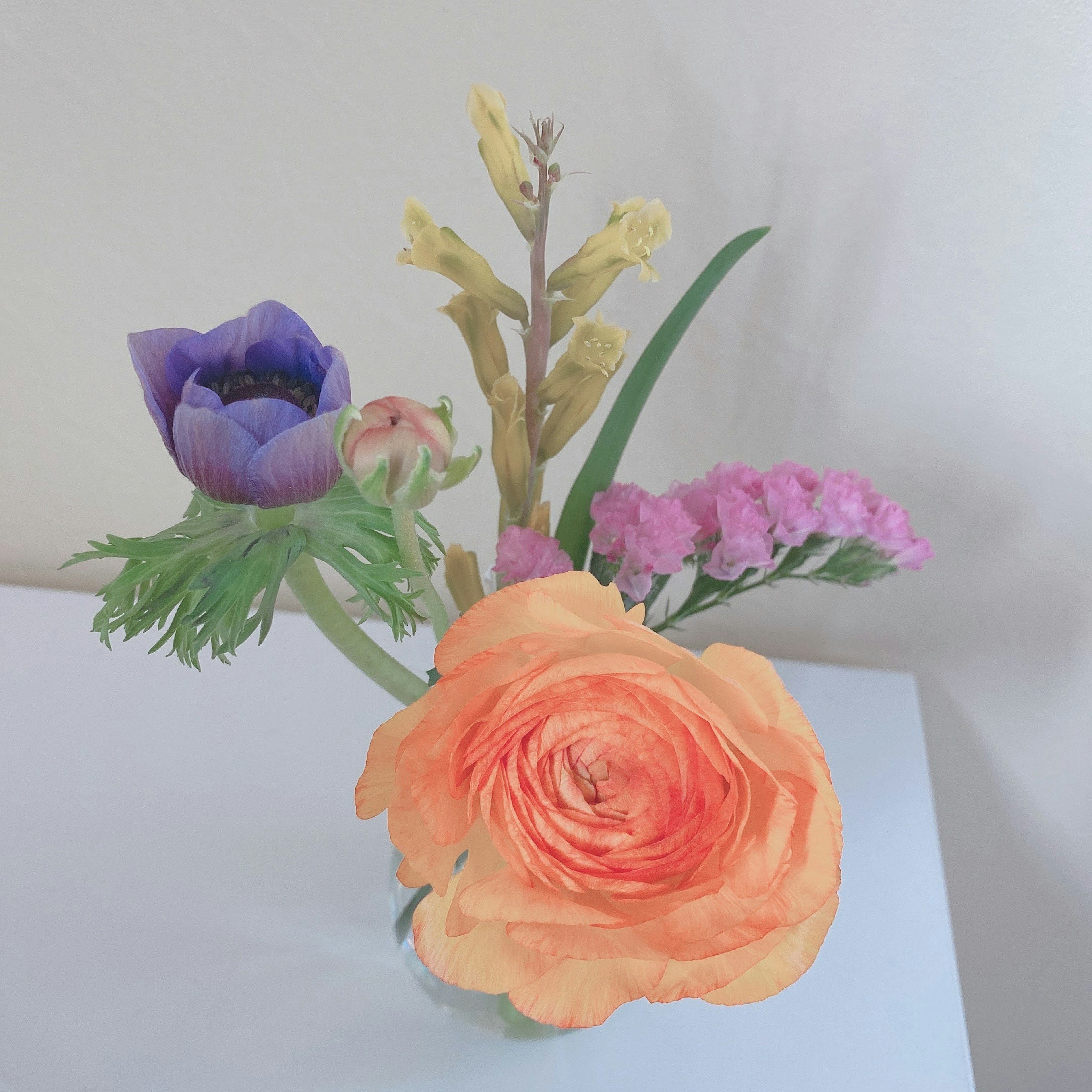 A bouquet featuring orange ranunculus and purple flowers arranged on a table