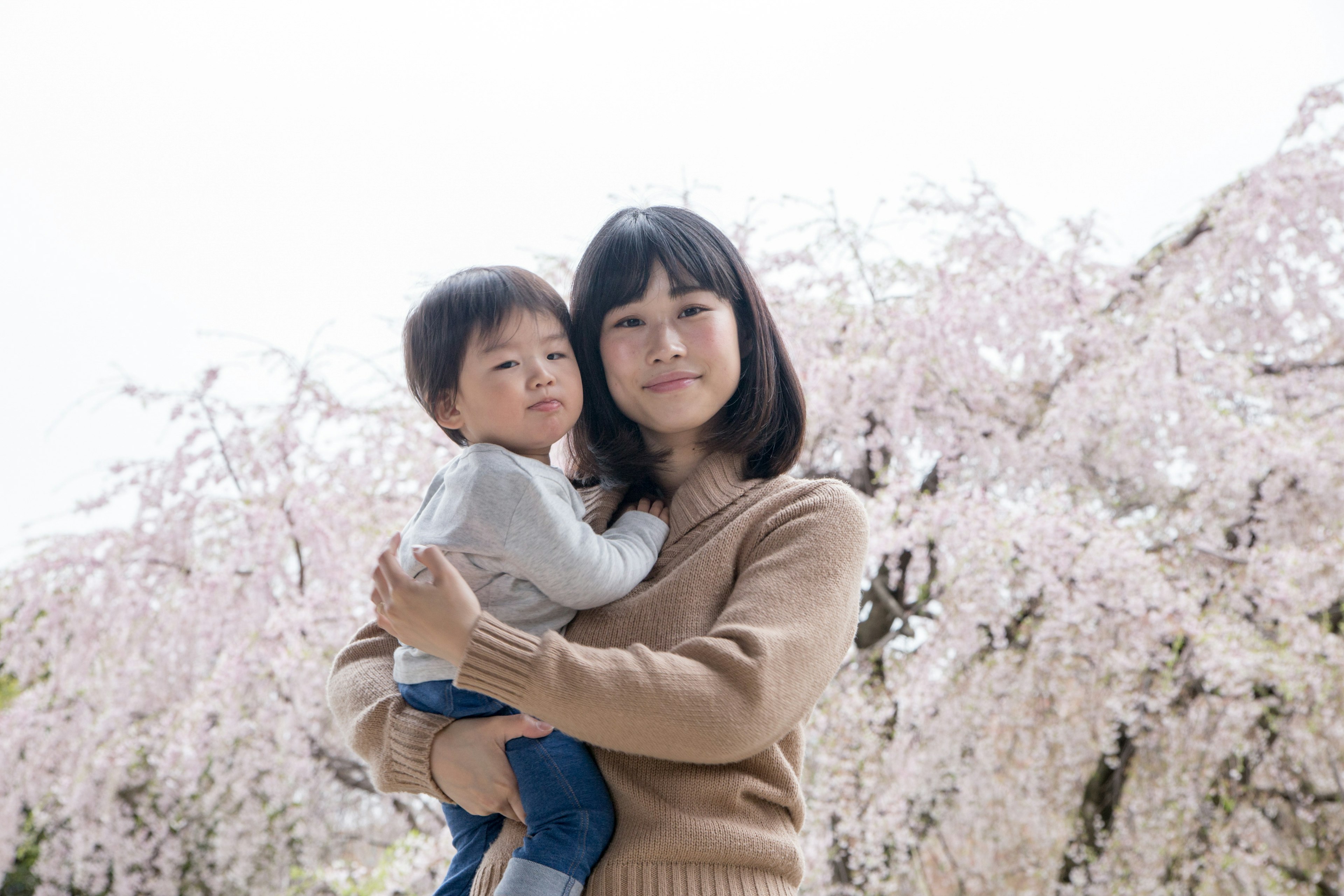 Une femme tenant un enfant devant des cerisiers en fleurs