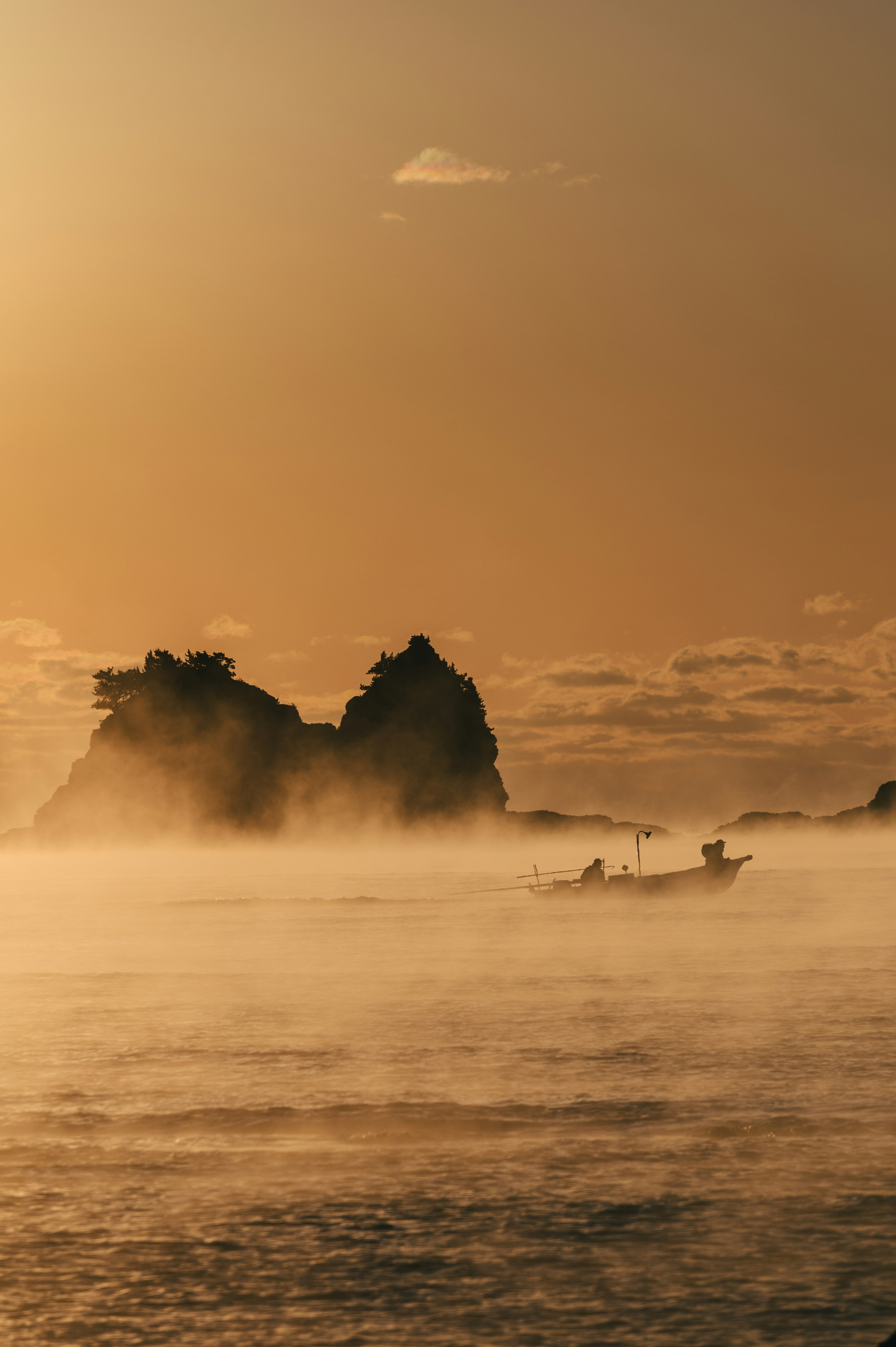 Paisaje marino brumoso con rocas en silueta y un resplandor de atardecer