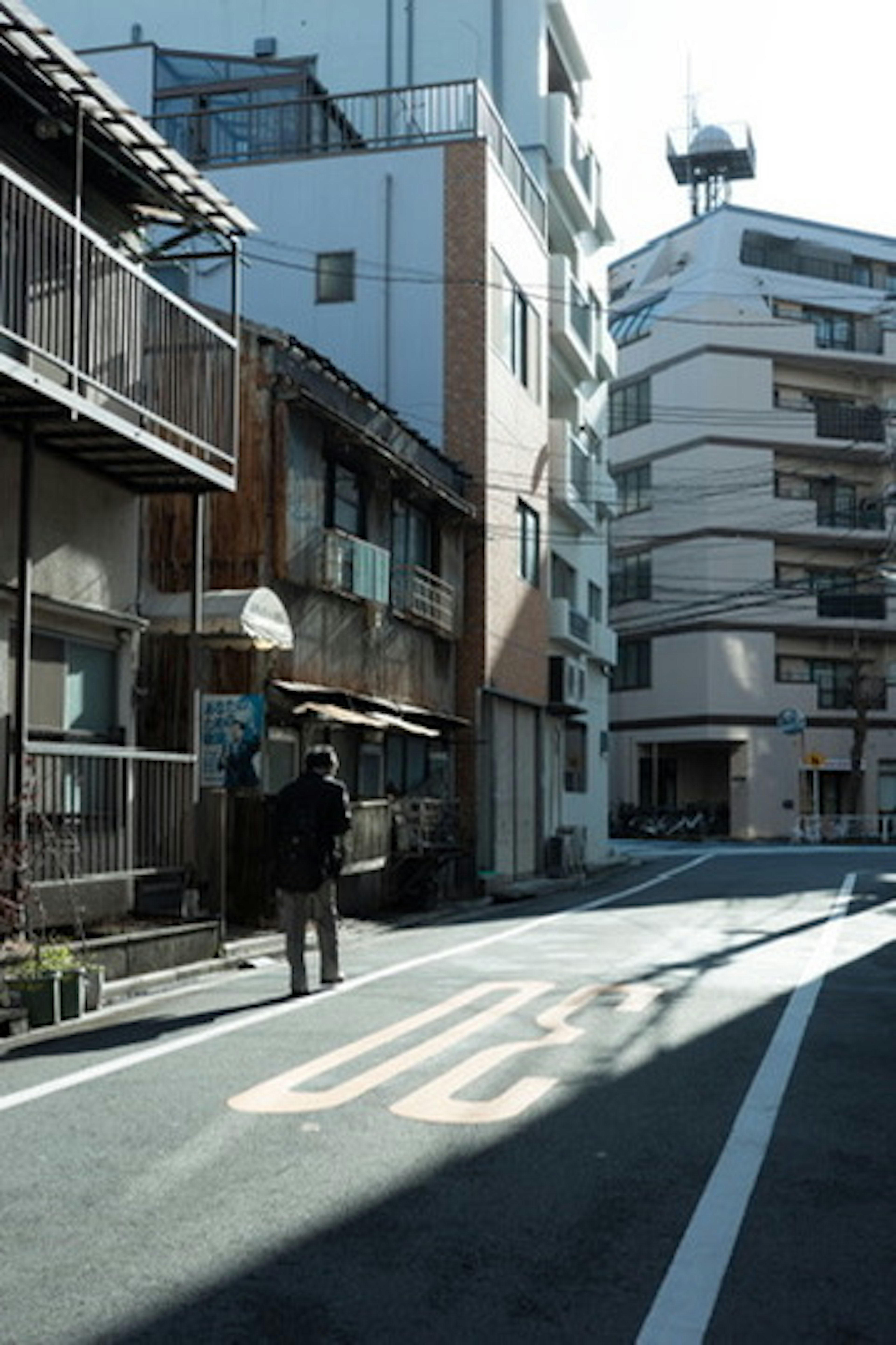 A narrow street with a person standing and old buildings lined up