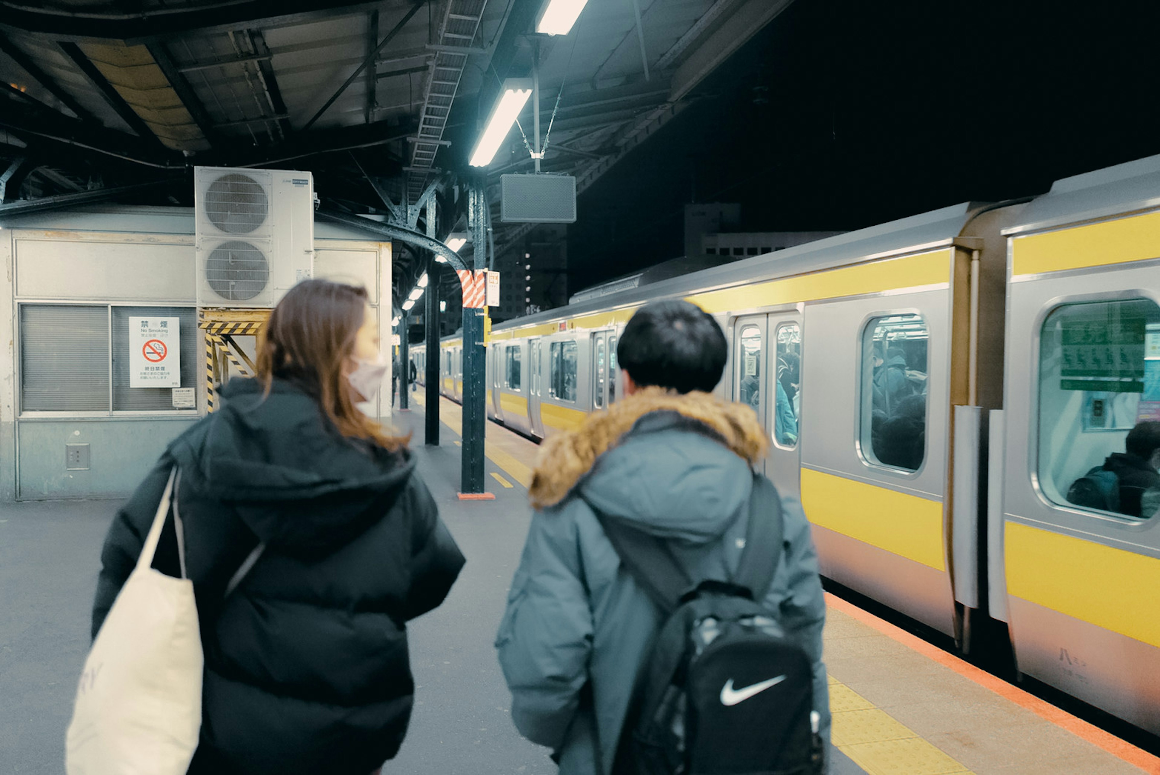 Zwei junge Menschen warten nachts auf einem Bahnsteig