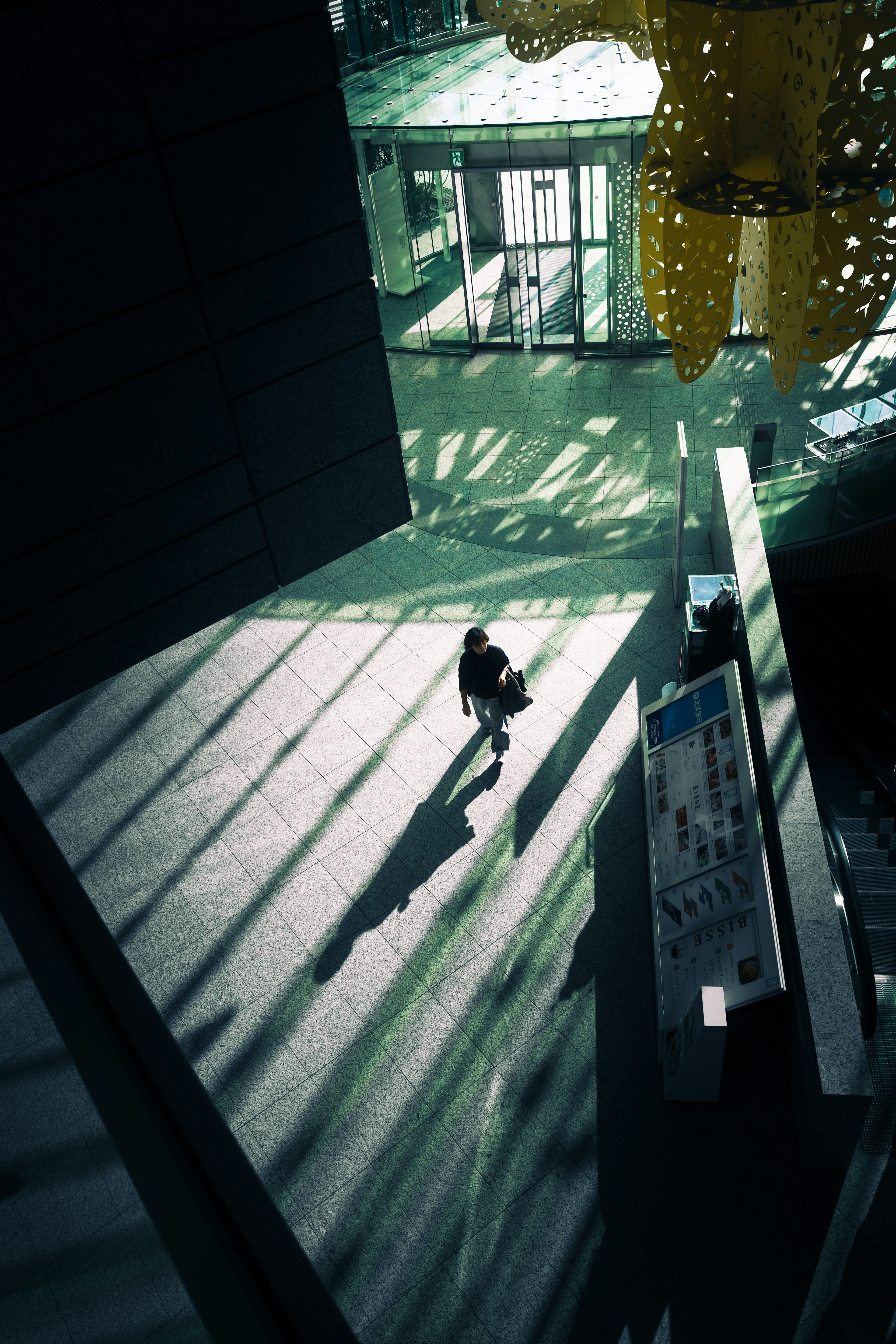 A person walking through shadows and light patterns in a modern building interior