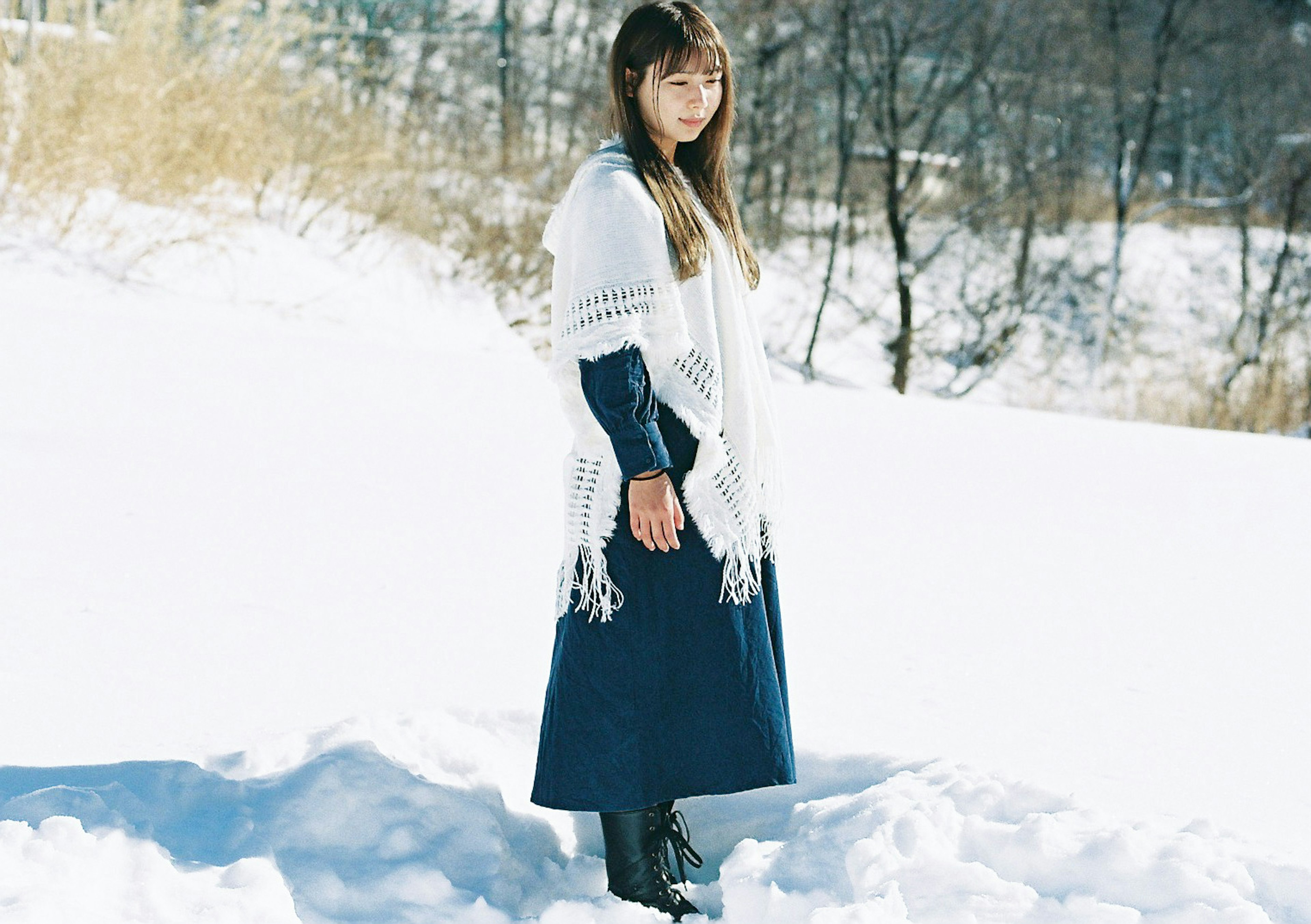 Una mujer de pie en la nieve con un vestido azul oscuro y un chal blanco