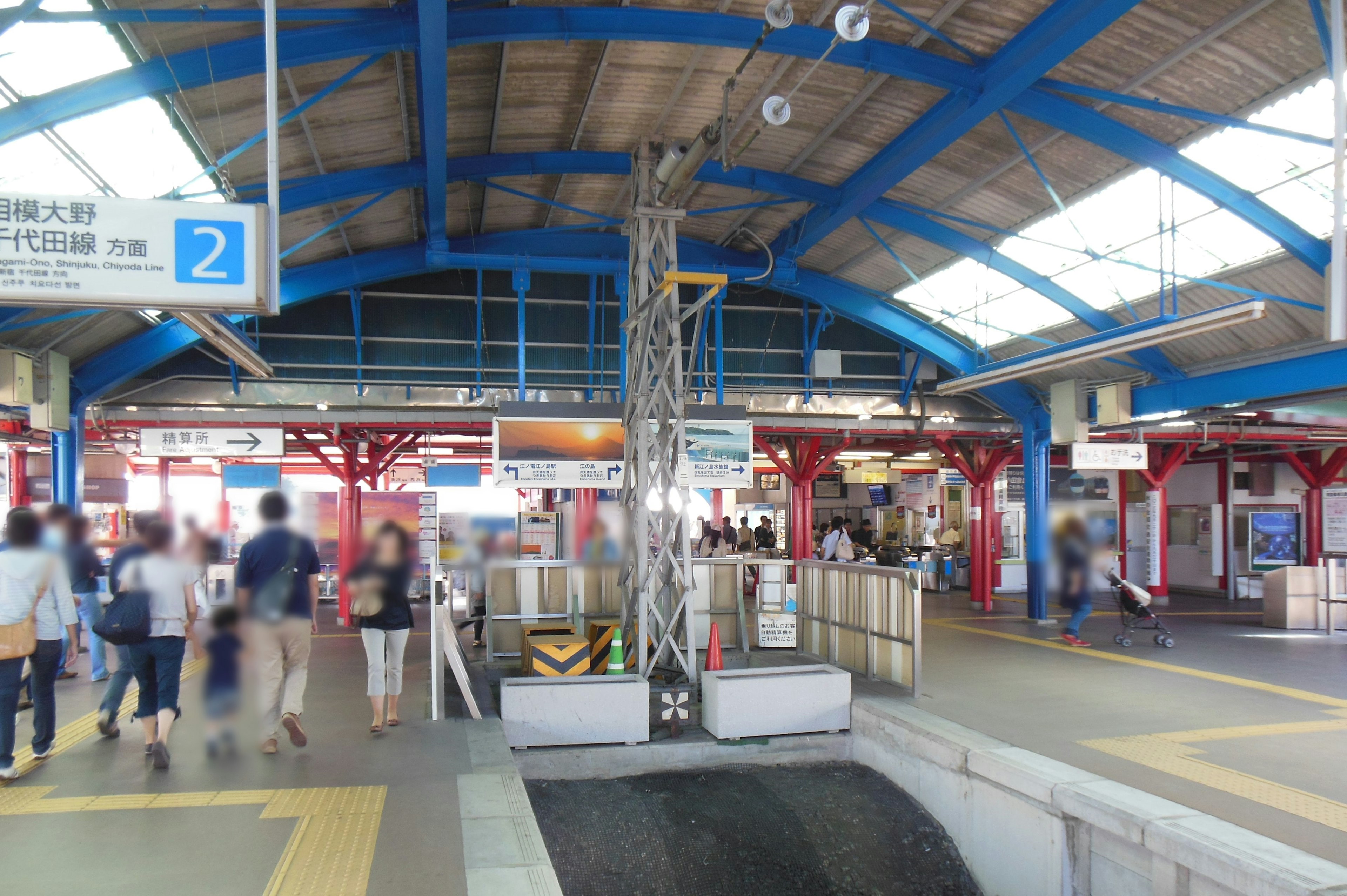 Interior of a train station with a blue roof many people walking around visible platforms and signs