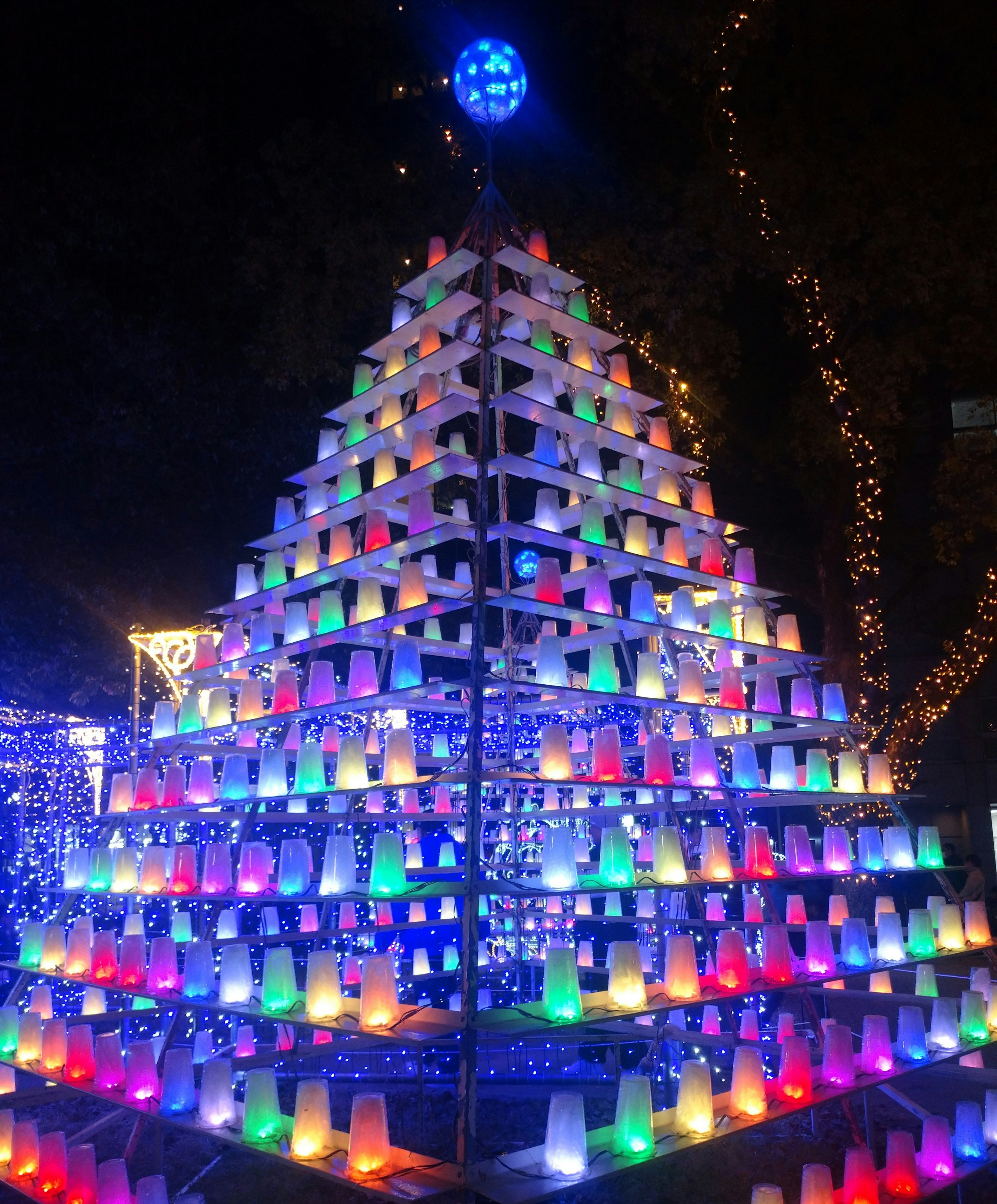 Künstlerischer Weihnachtsbaum aus bunten Bechern, der nachts beleuchtet ist