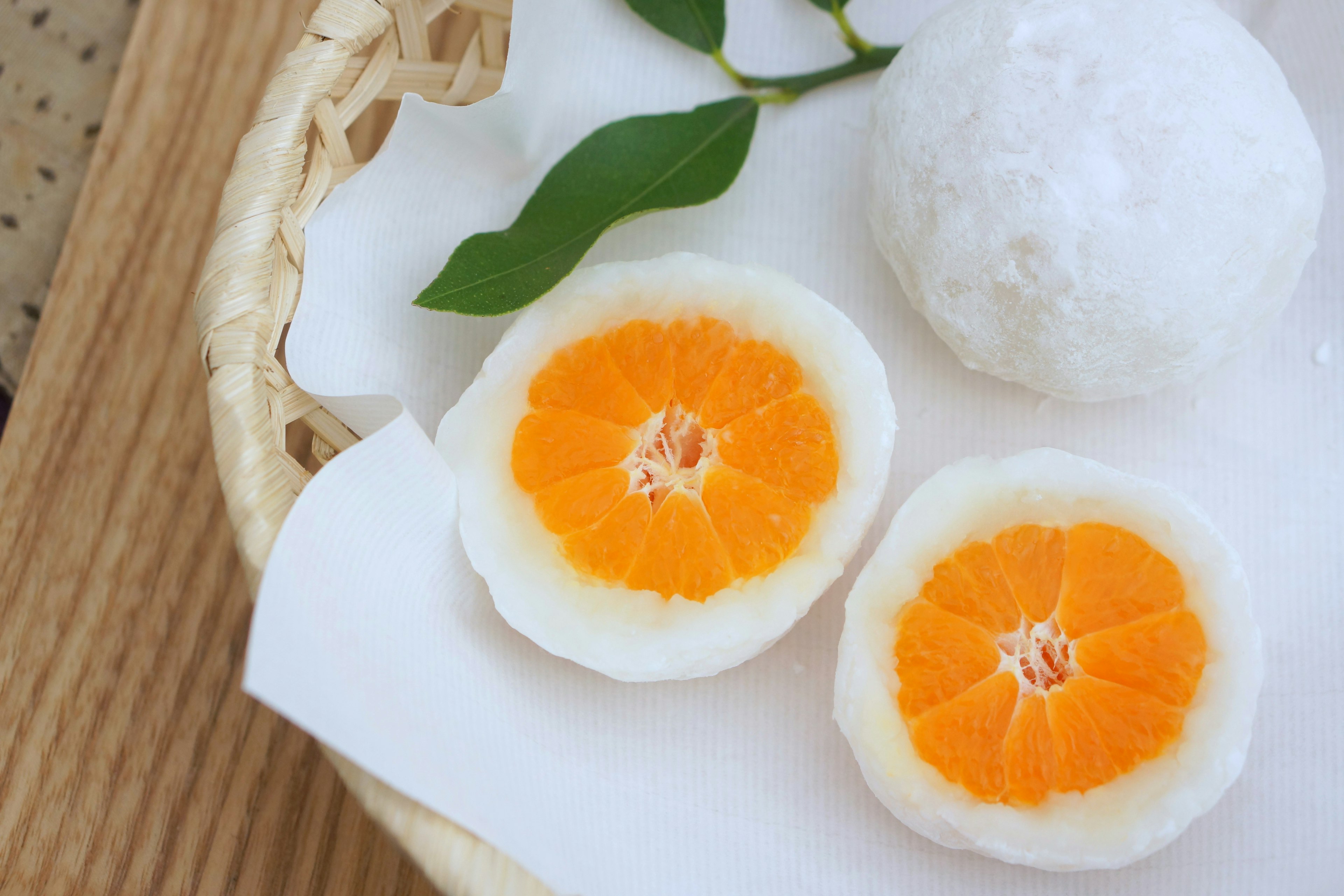 Rebanadas de mochi blanco mostrando fruta naranja en el interior y un mochi redondo descansando en una canasta de bambú