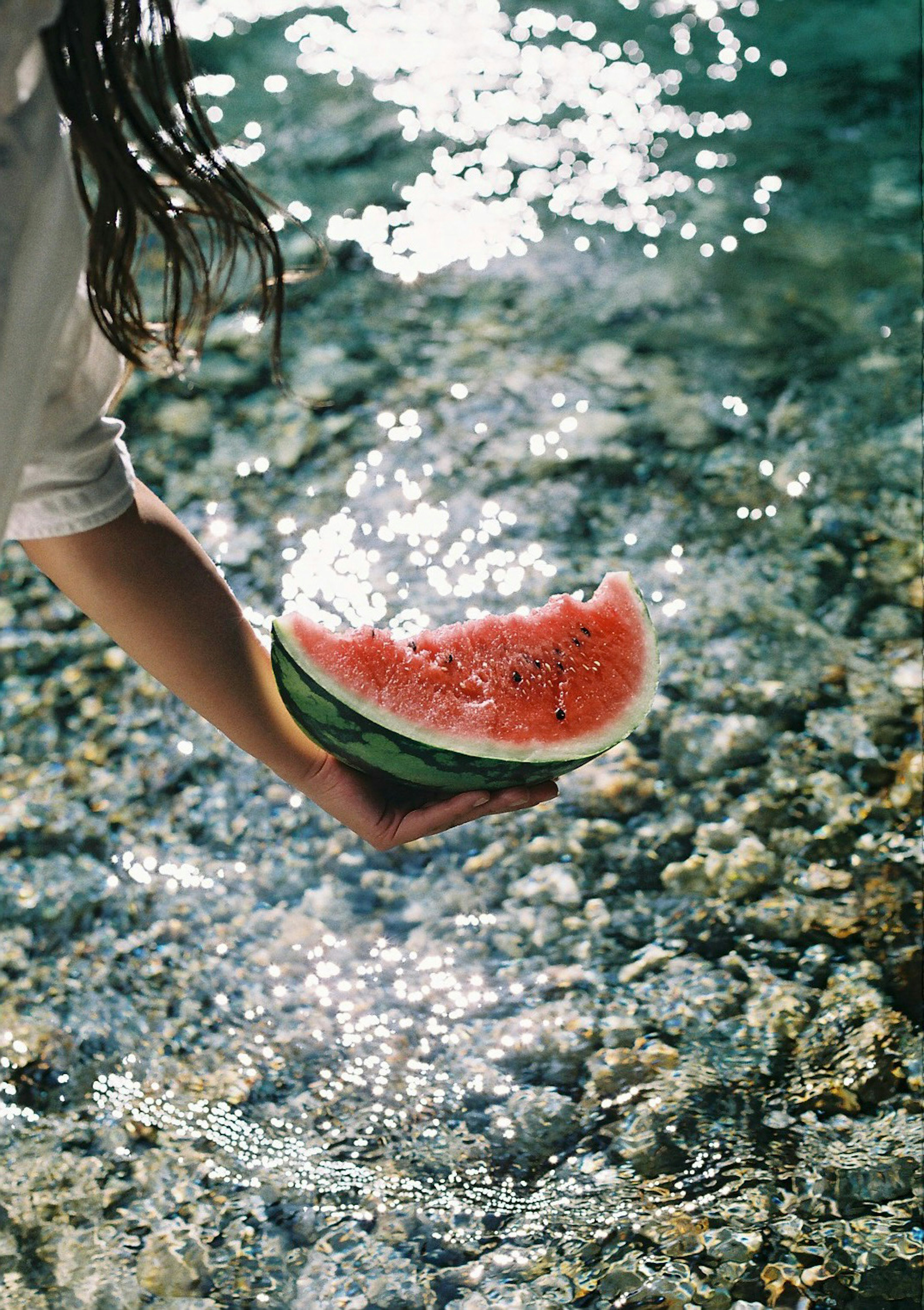 Mano che tiene una fetta di anguria sopra l'acqua luccicante