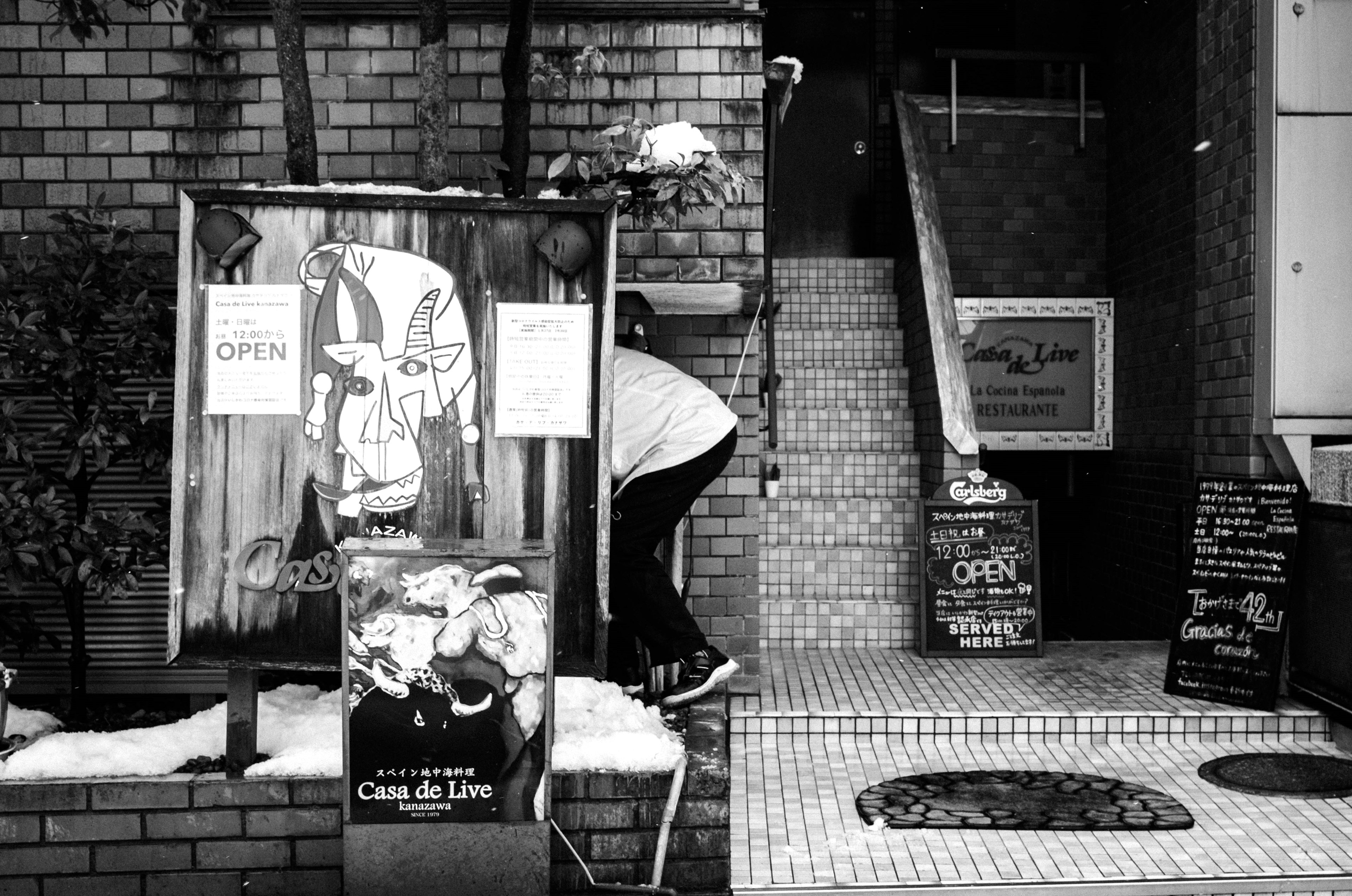 Black and white exterior of a shop entrance with several signs displayed