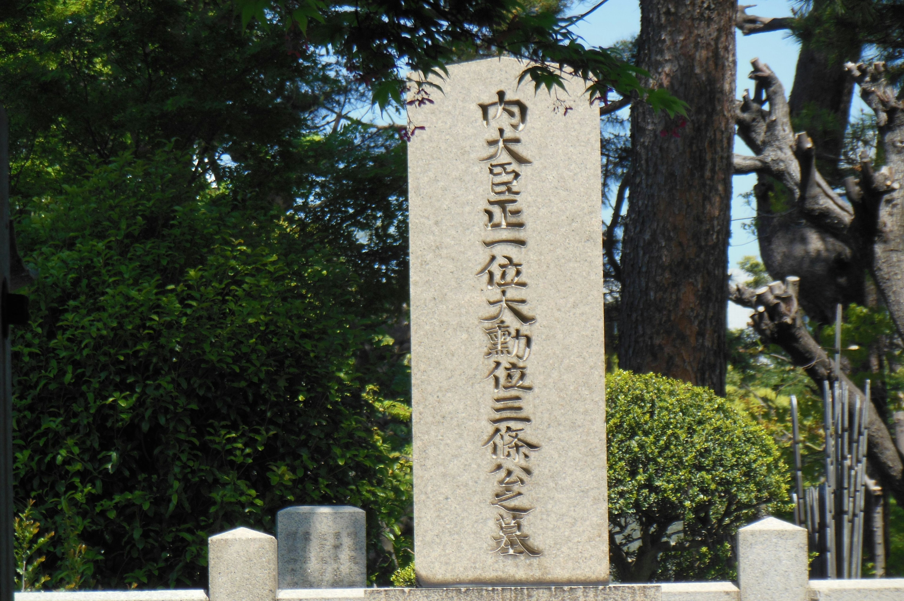 Monumento de piedra con texto japonés en un entorno de parque verde