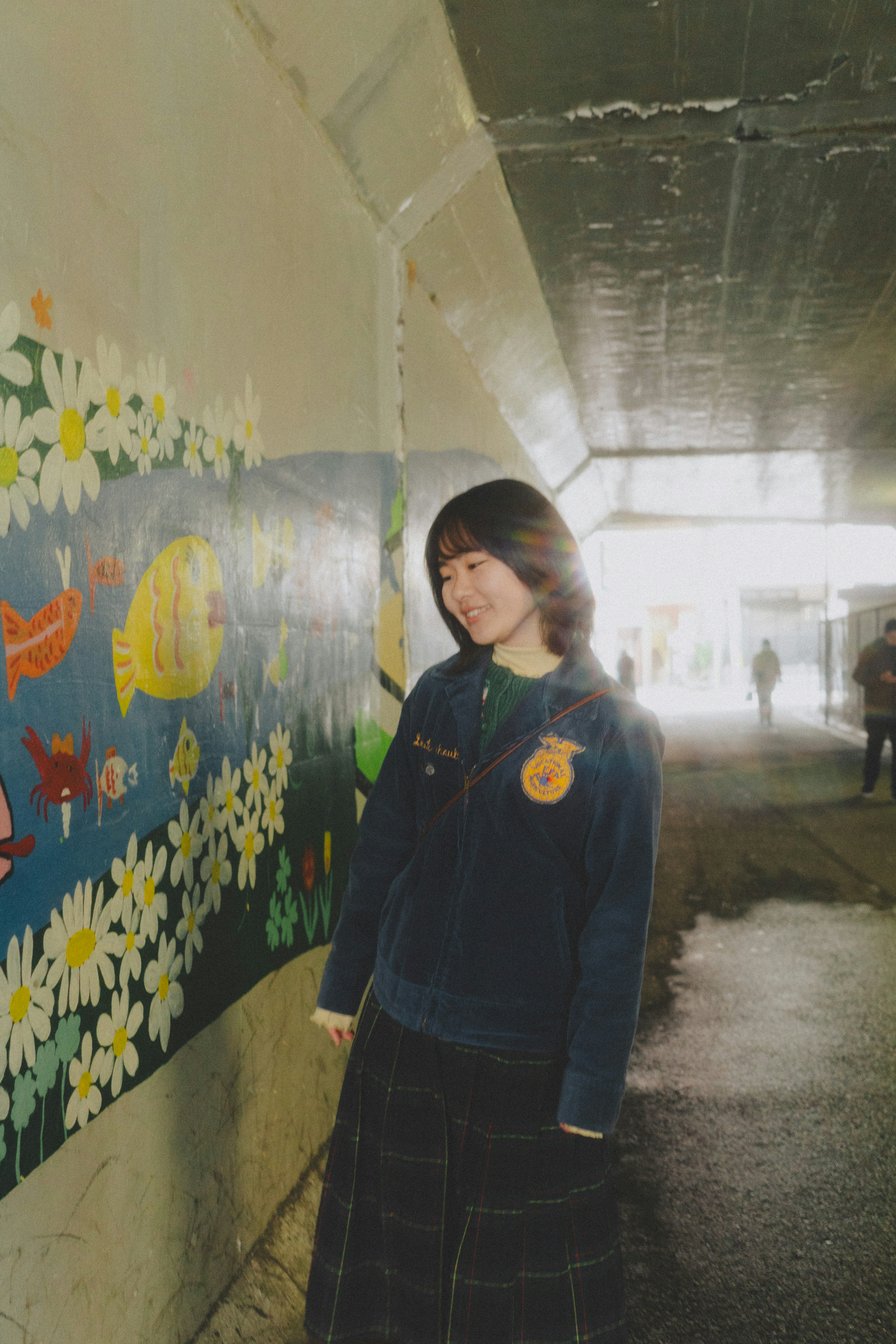 Una estudiante de pie en un túnel con un mural de flores y peces