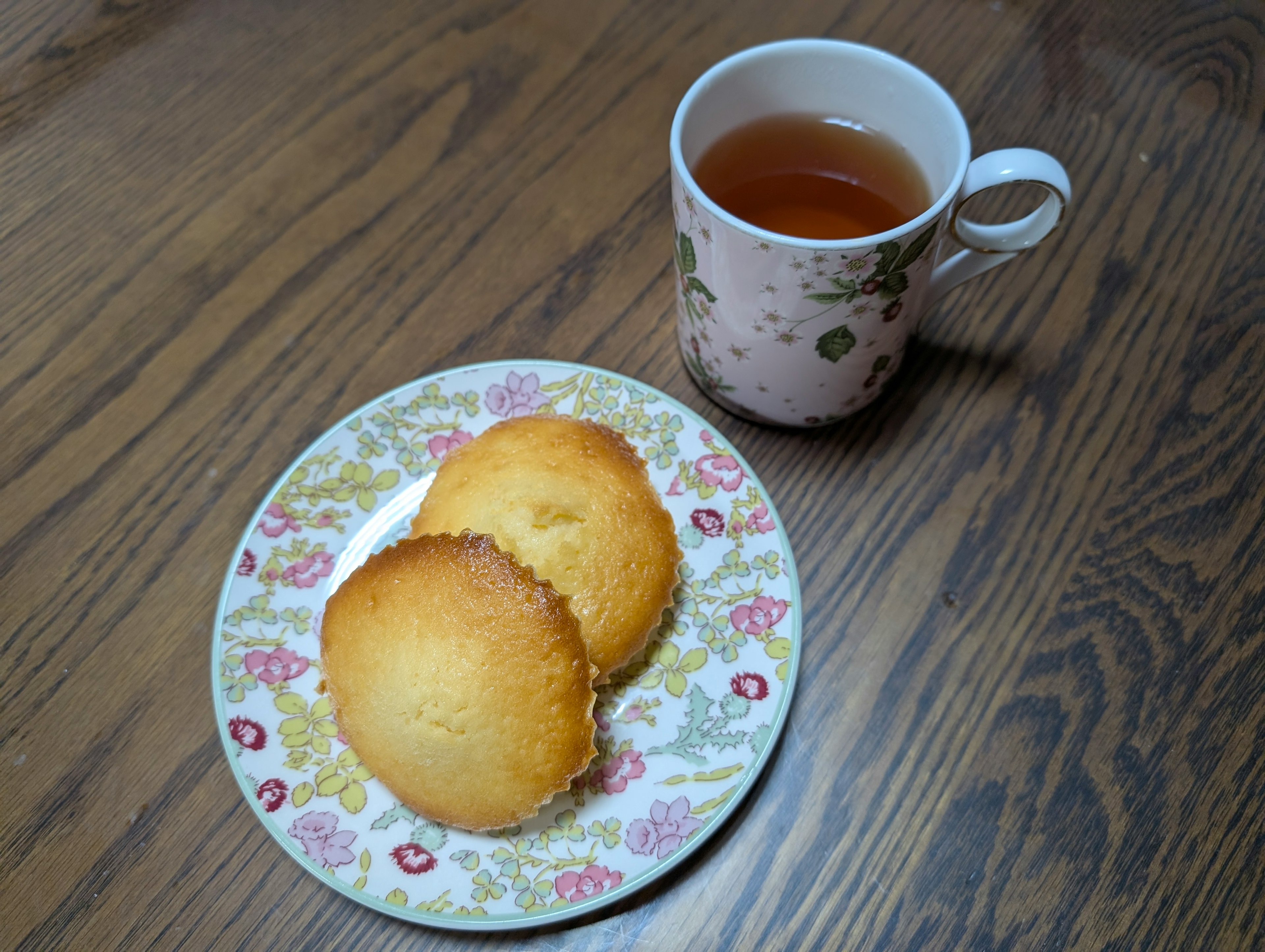 Une assiette de deux madeleines à côté d'une tasse de thé sur une table en bois