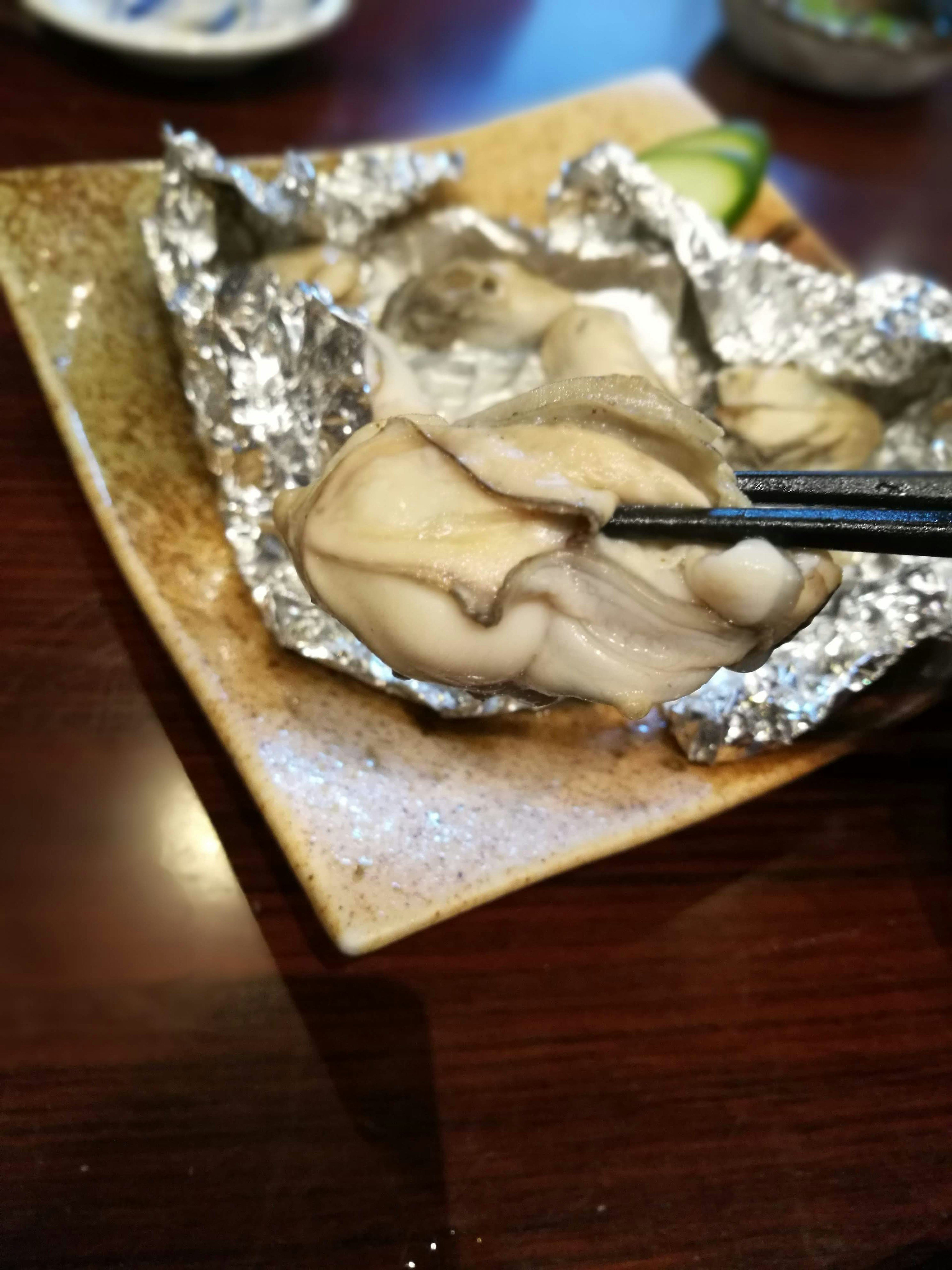 Huître crue sur une assiette enveloppée dans du papier d'aluminium tenue avec des baguettes