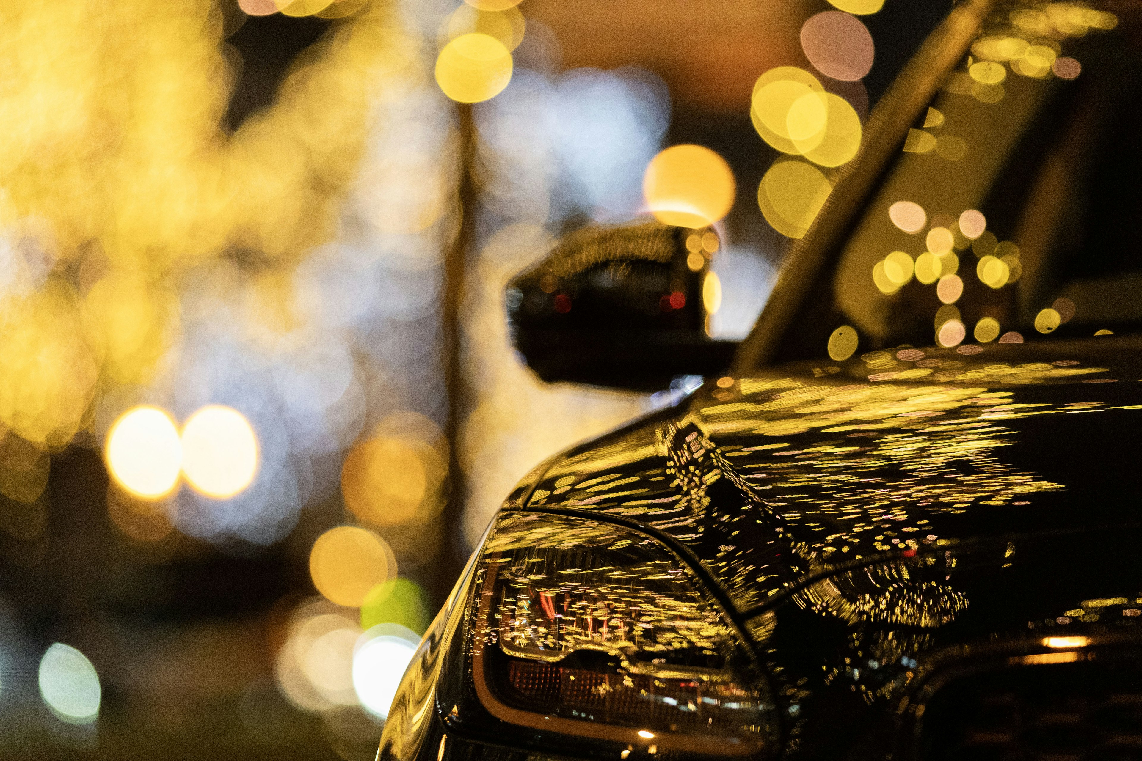 Close-up of a black car reflecting bright bokeh lights at night