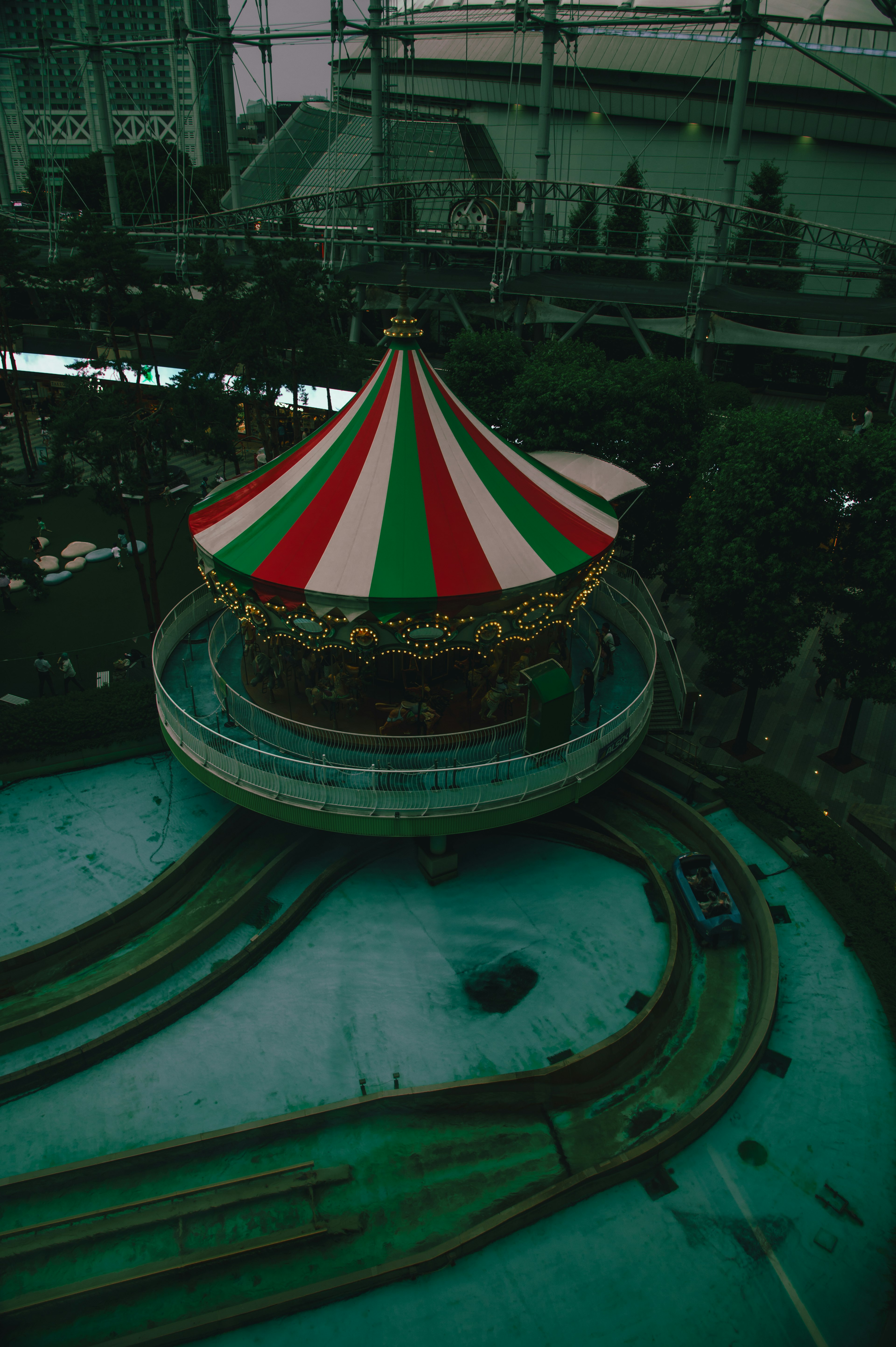 Carrusel de parque de diversiones con techo a rayas verdes y rojas sobre una pista de agua