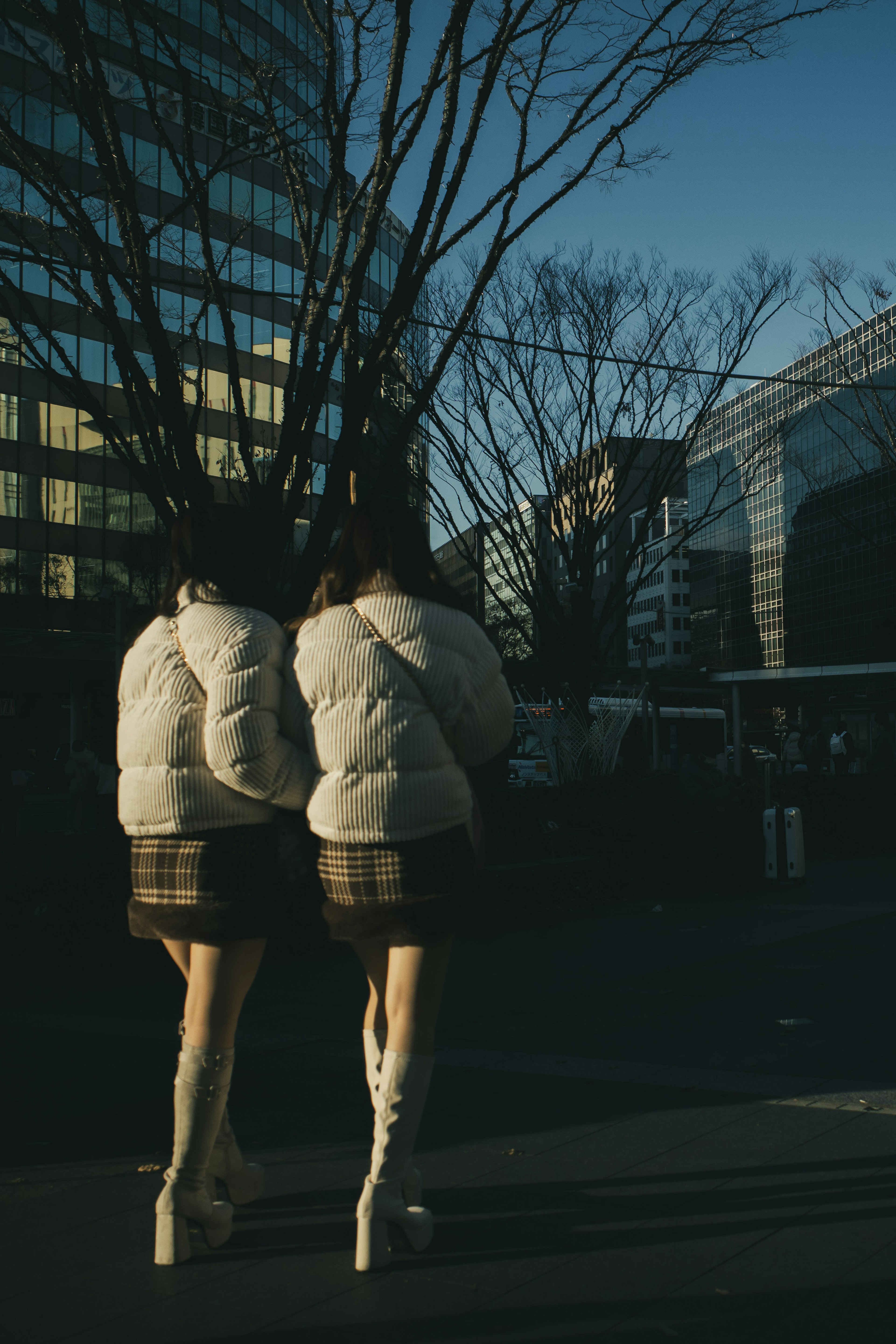 Two women wearing white jackets and plaid mini skirts in an urban setting