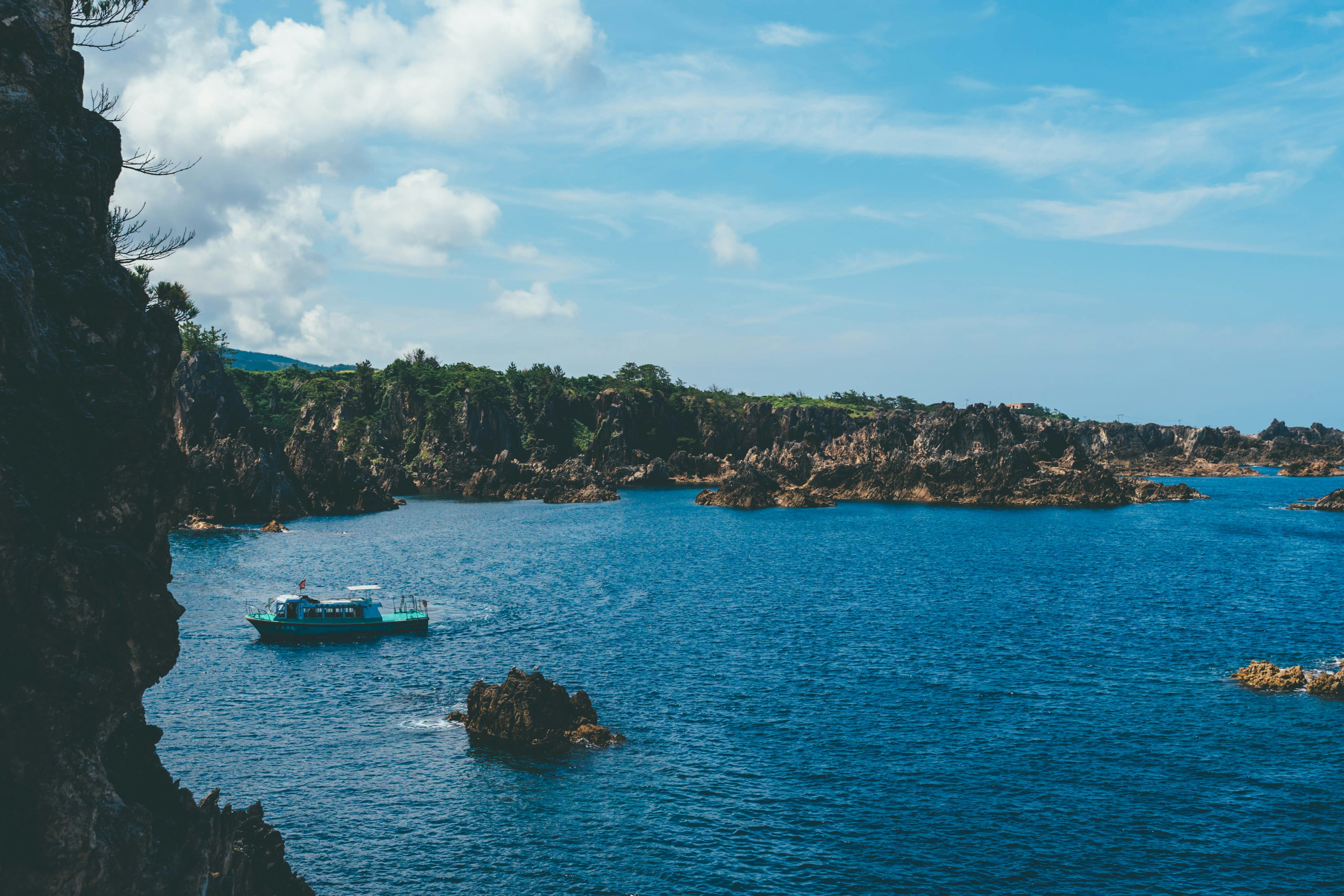 Pemandangan laut biru dengan batu-batu tersebar sebuah perahu berlayar di perairan