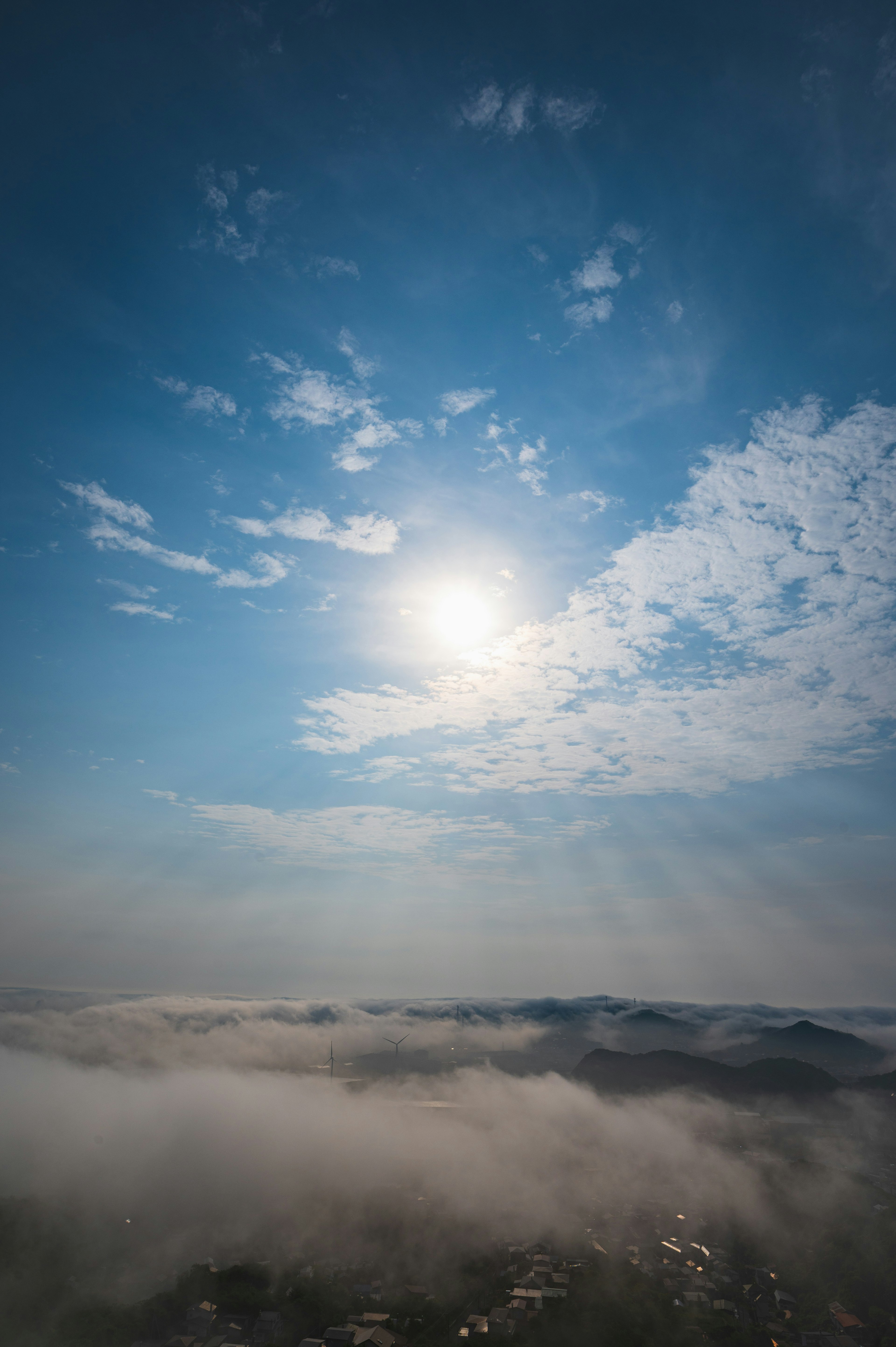 Un paesaggio nebbioso sotto un cielo blu con nuvole e sole