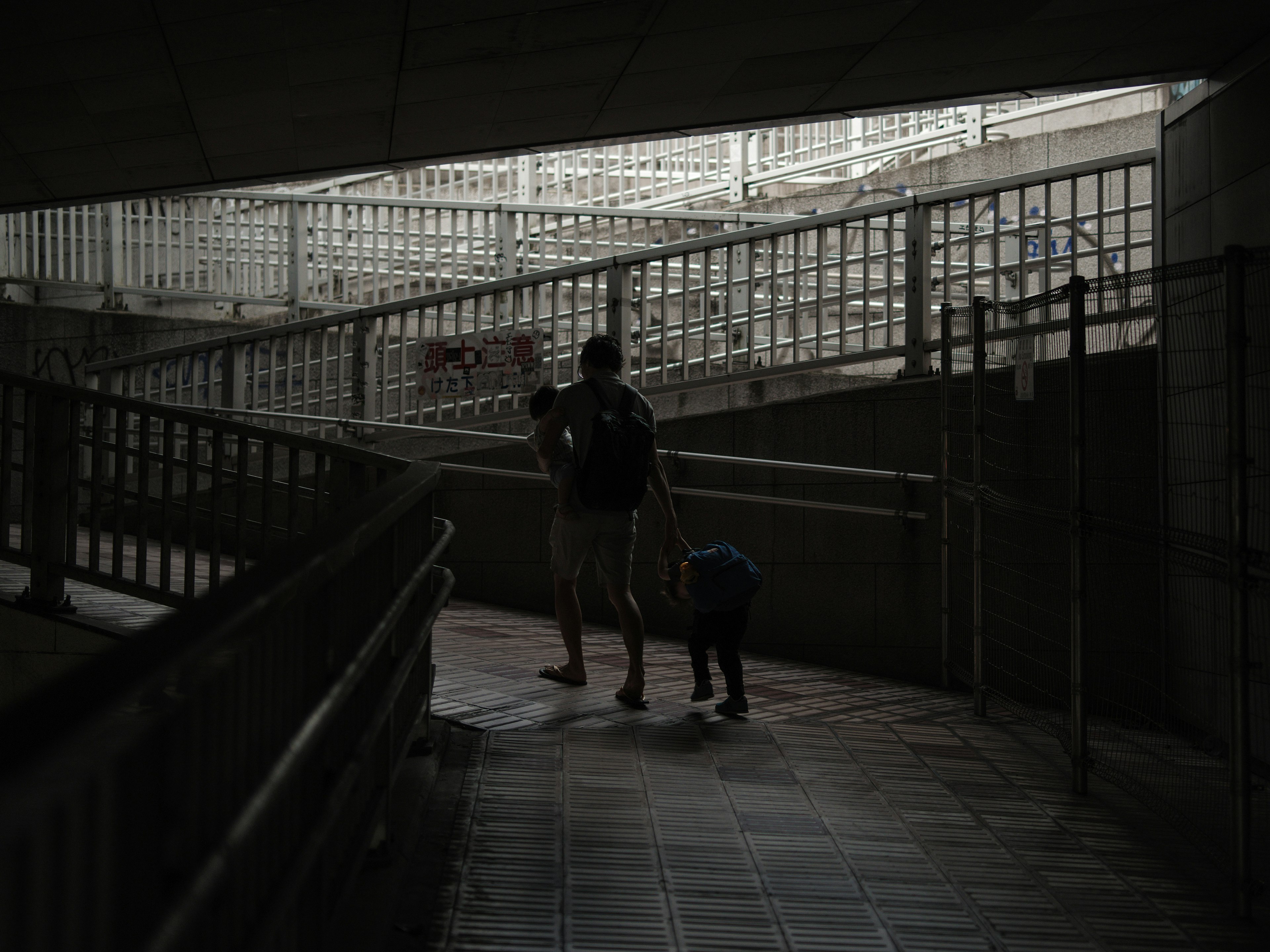 Silhouette d'un parent et d'un enfant marchant dans un couloir sombre avec des rampes en métal